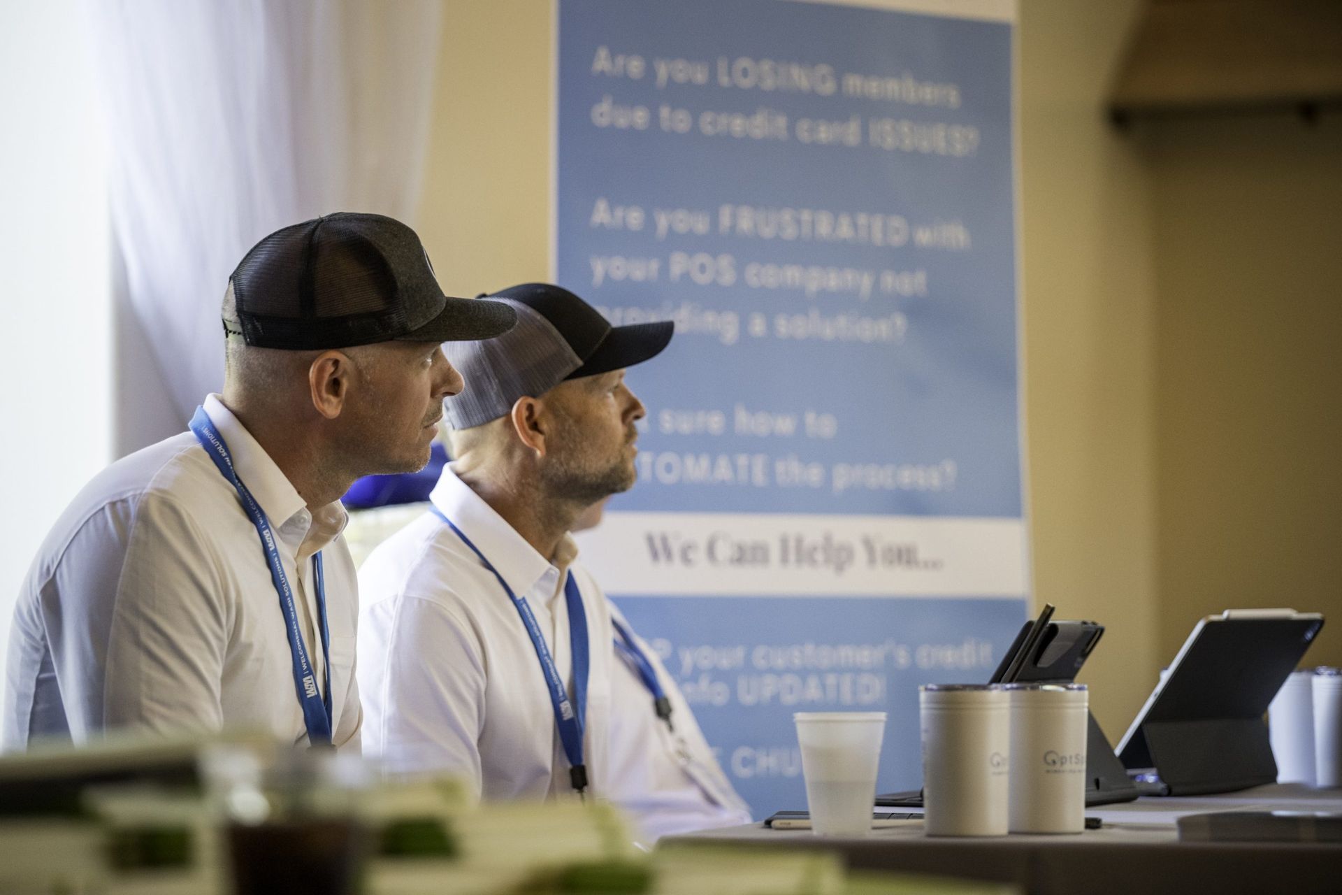 Two men are sitting at a table in front of a sign.