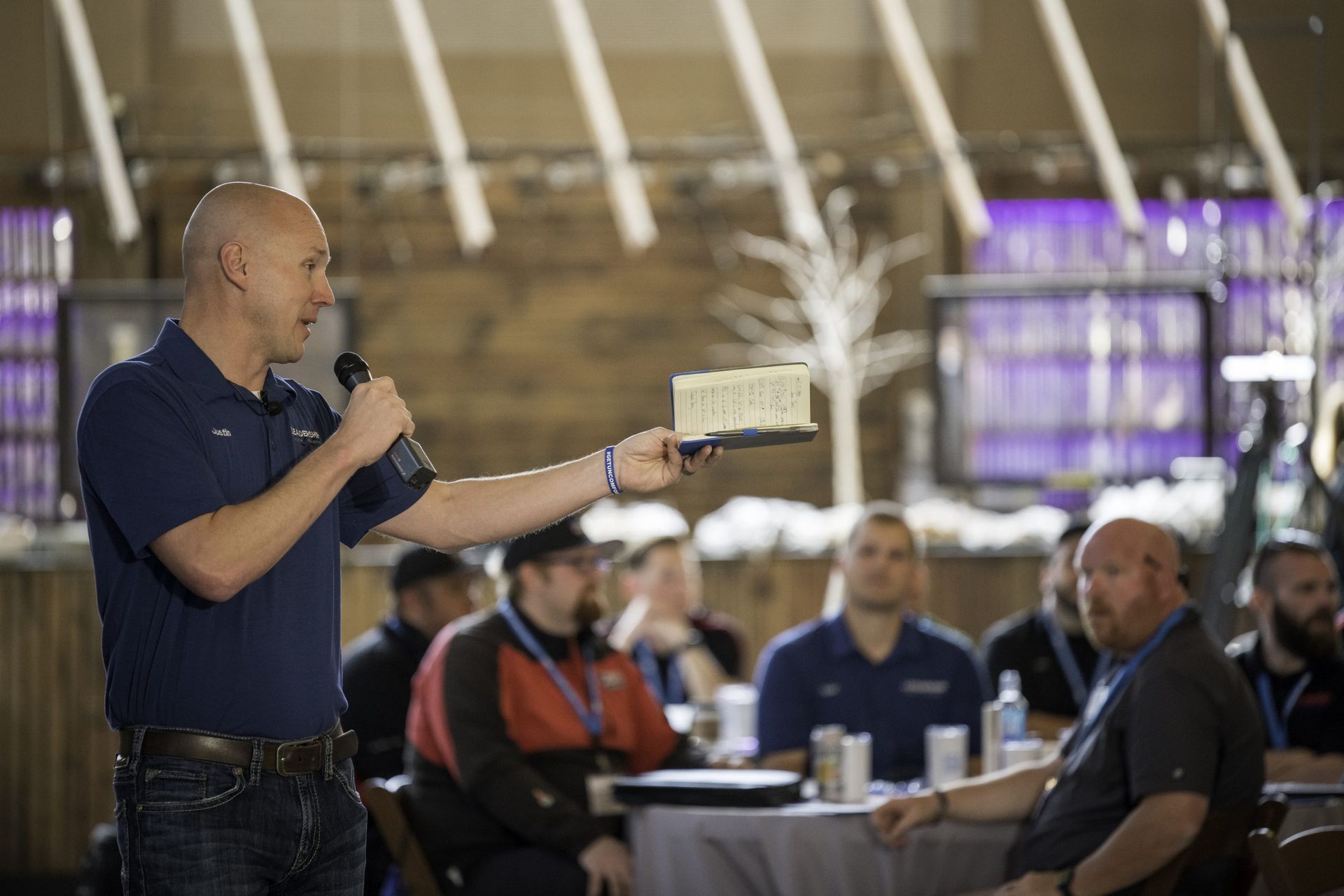 A man is holding a microphone and giving a presentation to a group of men.