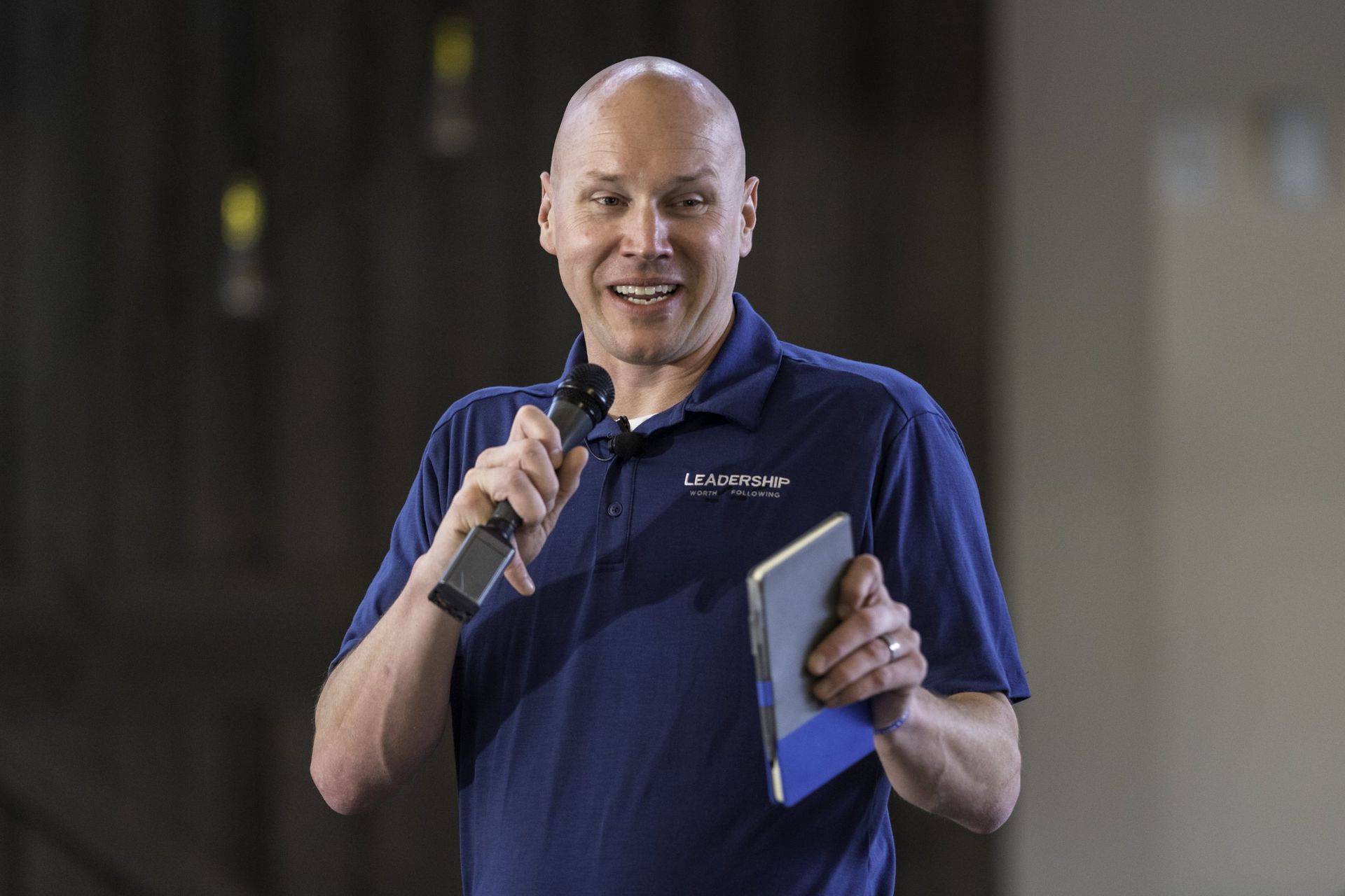 A man in a blue shirt is holding a microphone and a tablet.