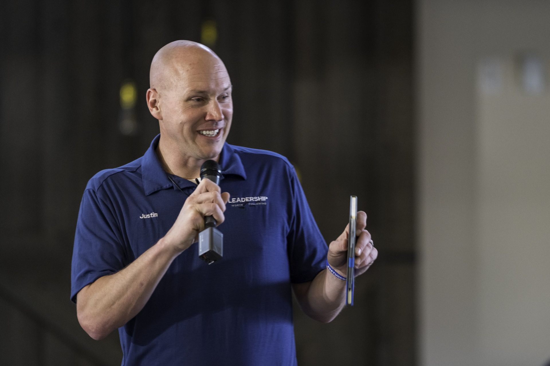 A man in a blue shirt is holding a microphone and a cell phone.