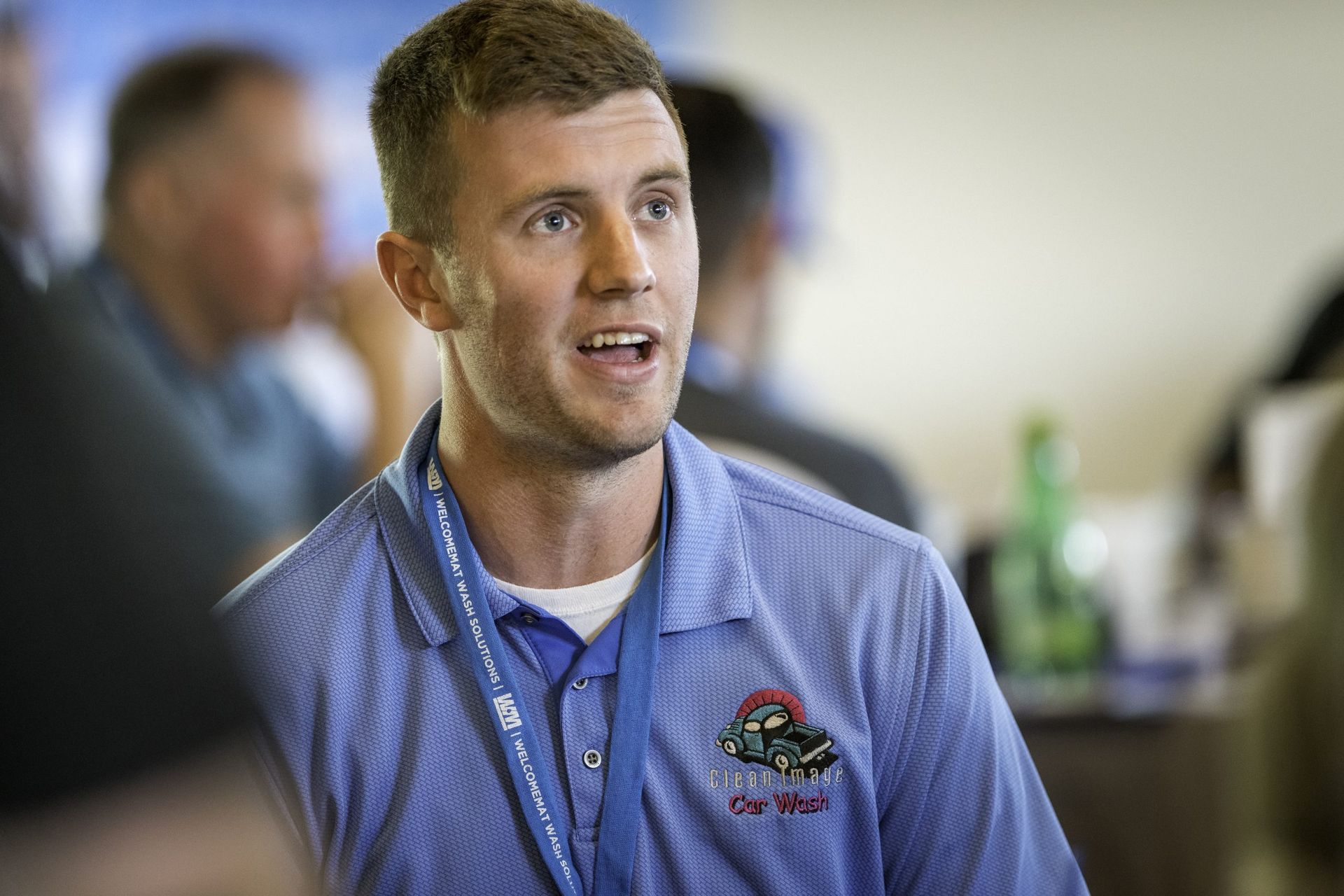 A man wearing a blue shirt with a lanyard around his neck is talking to a group of people.