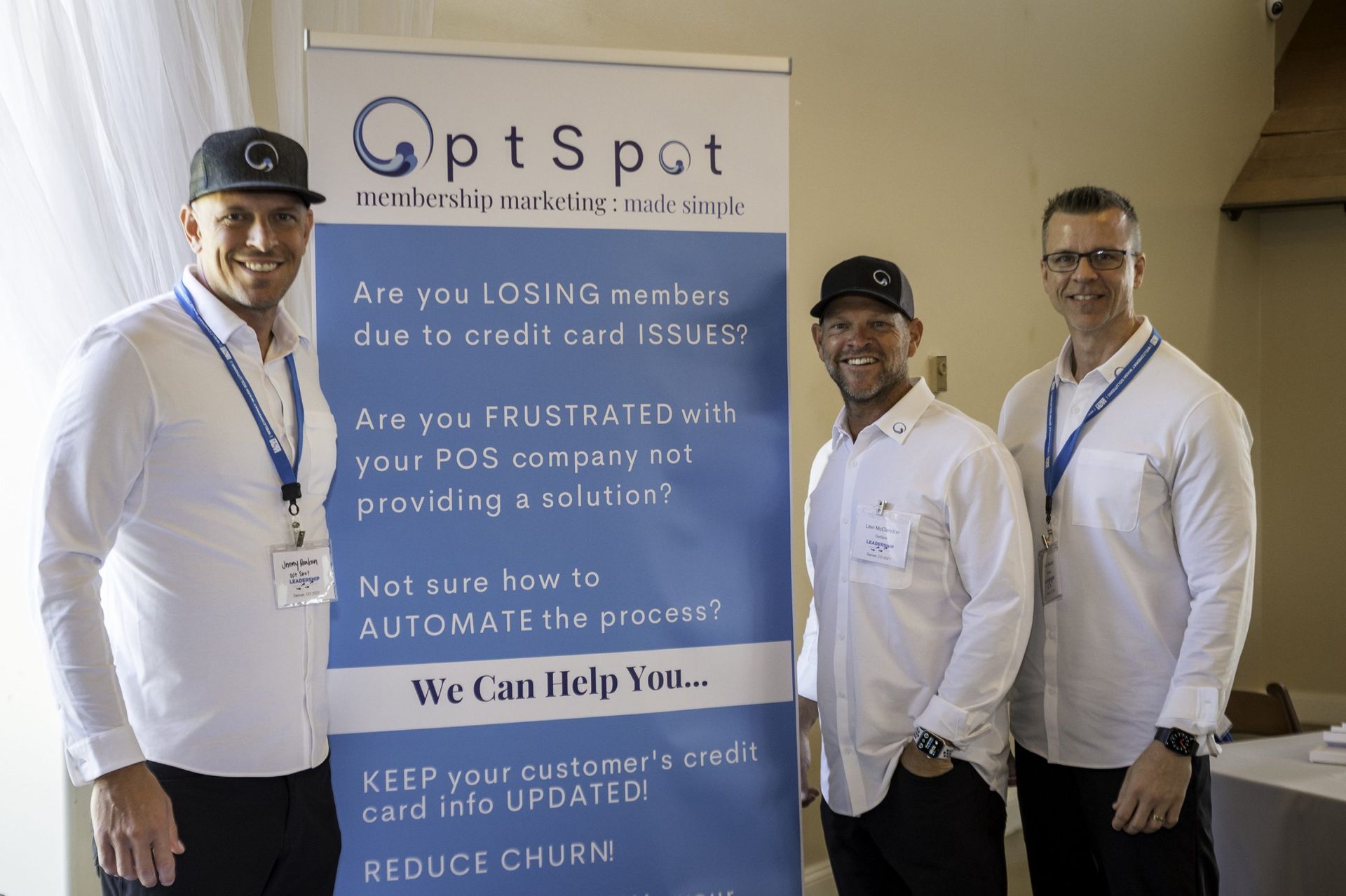 Three men are standing in front of a sign that says optspot.