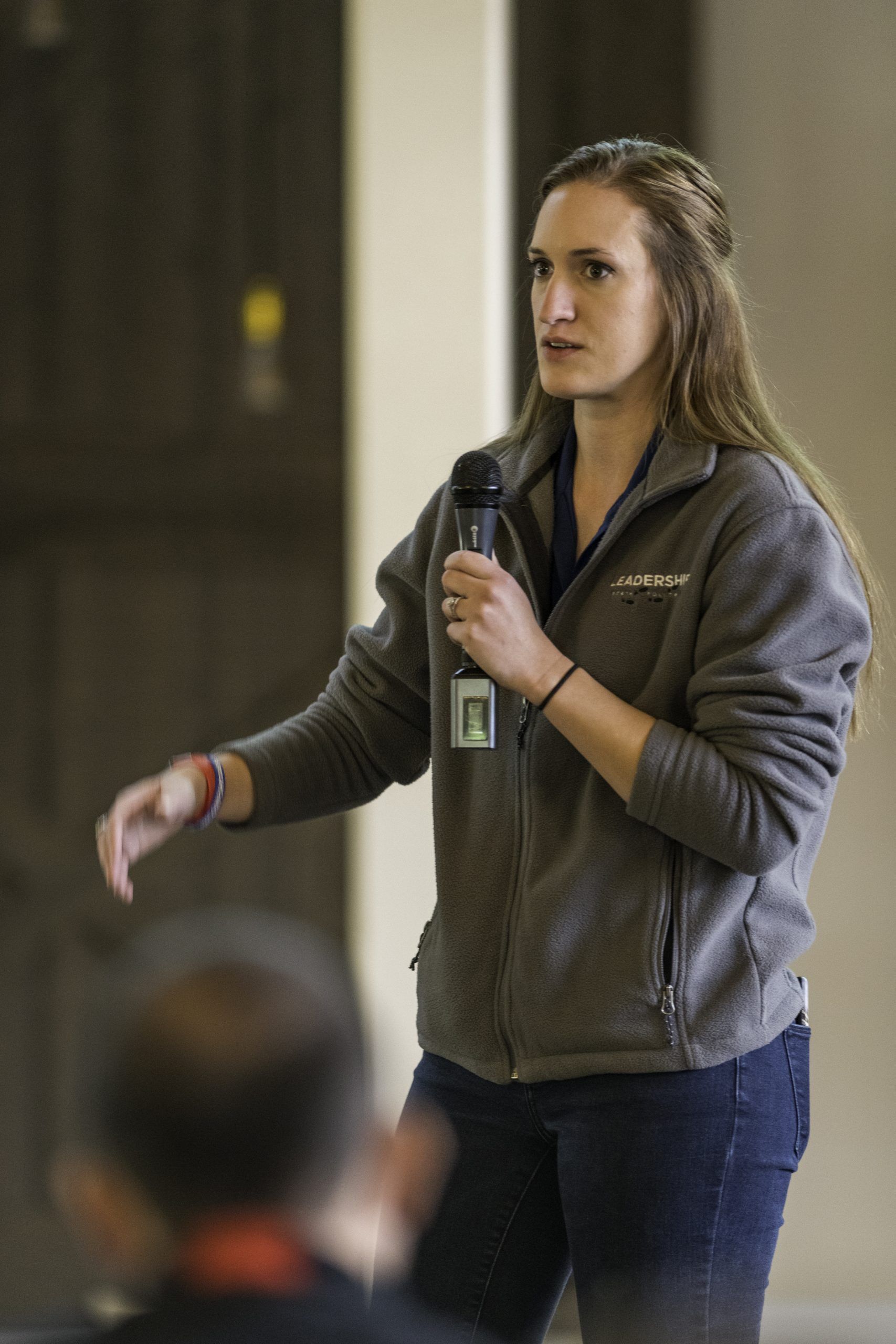 A woman in a columbia jacket is holding a microphone and talking to a group of people.