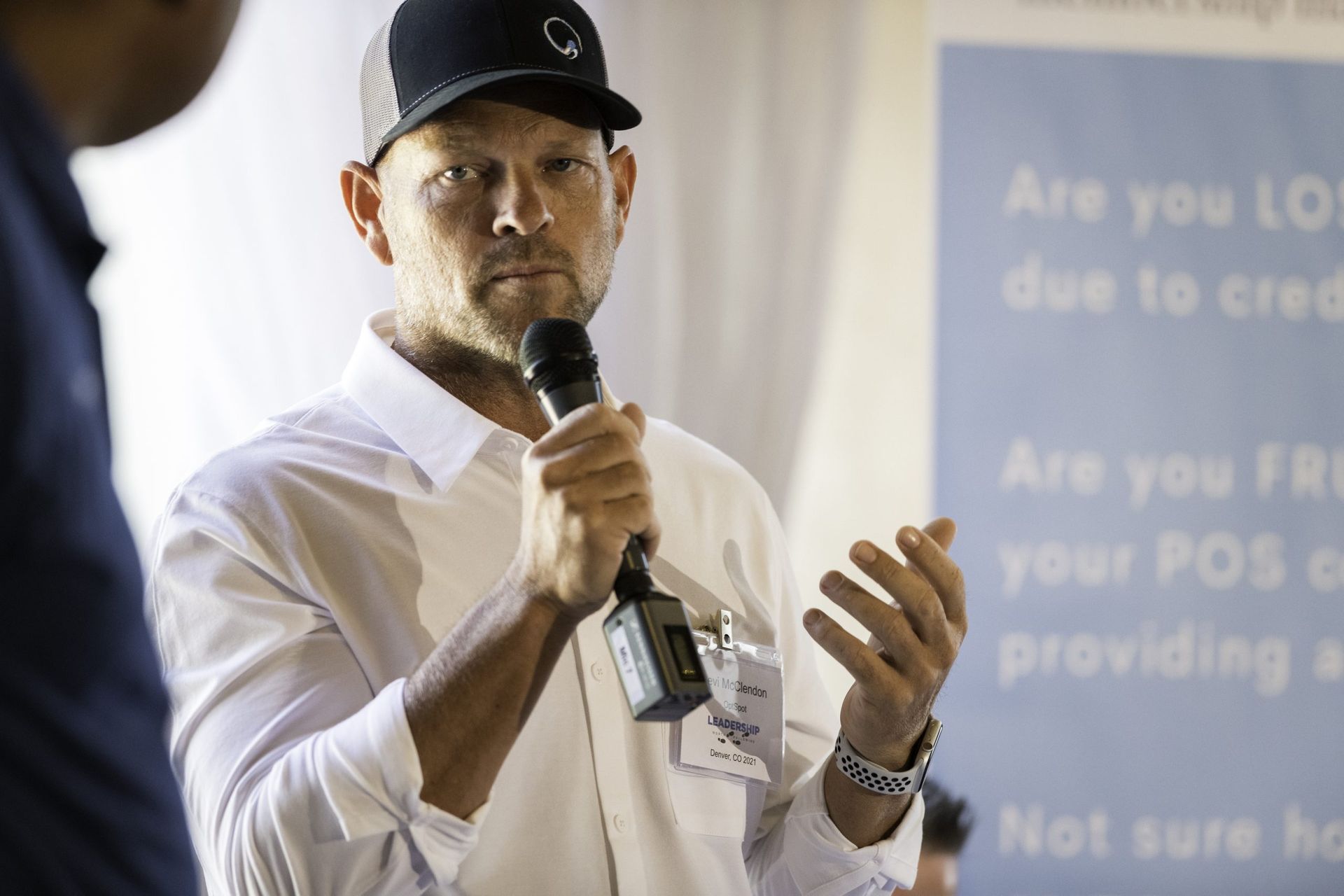 A man in a hat is holding a microphone and talking to another man.