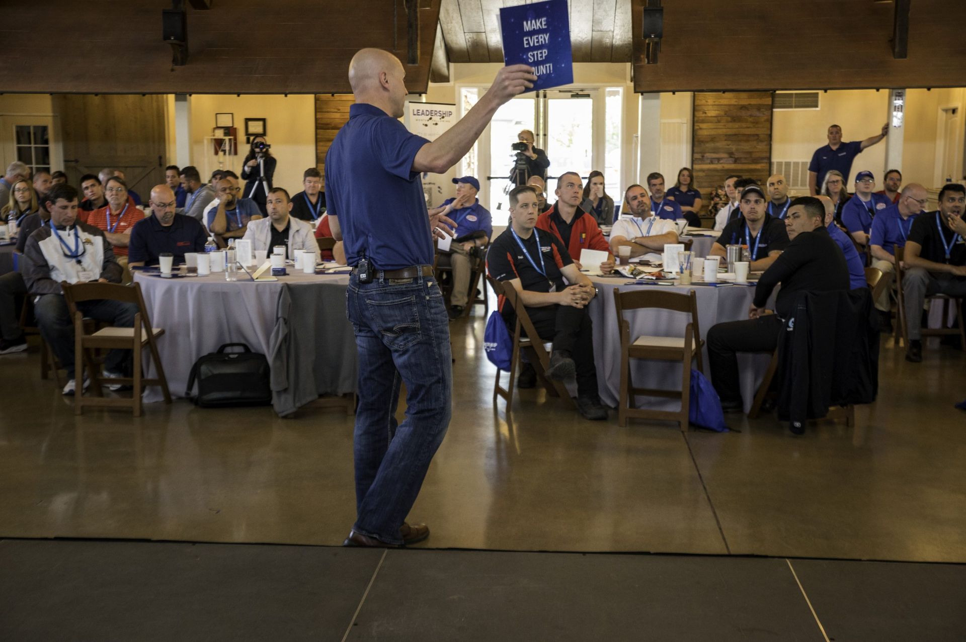 A man is giving a presentation to a group of people sitting at tables.