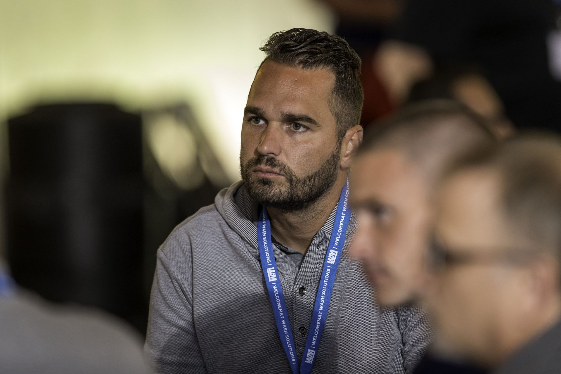 A man with a lanyard around his neck is sitting in a crowd of people.