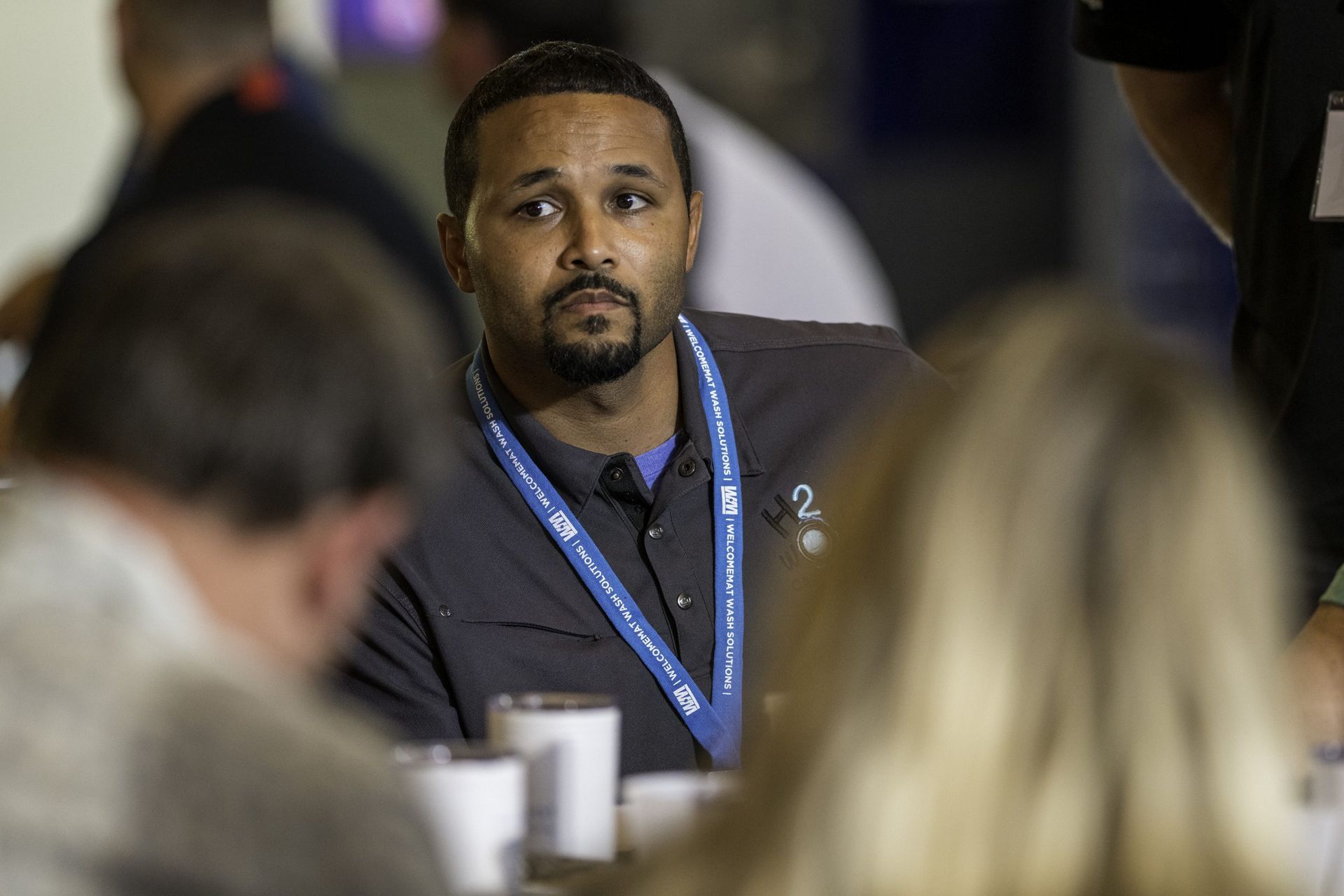 A man with a lanyard around his neck is sitting at a table with other people.