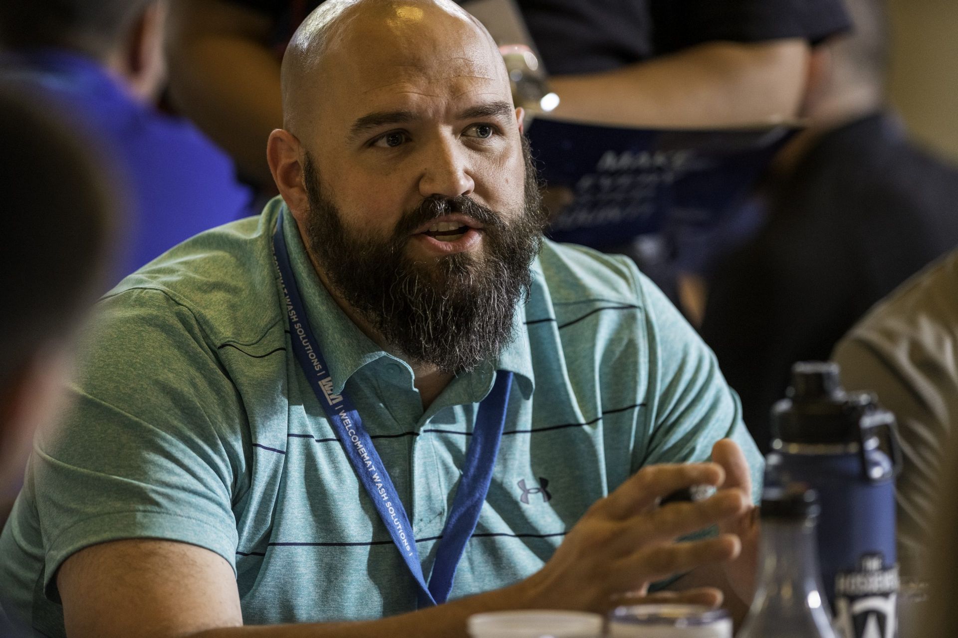 A bald man with a beard is sitting at a table talking to a group of people.