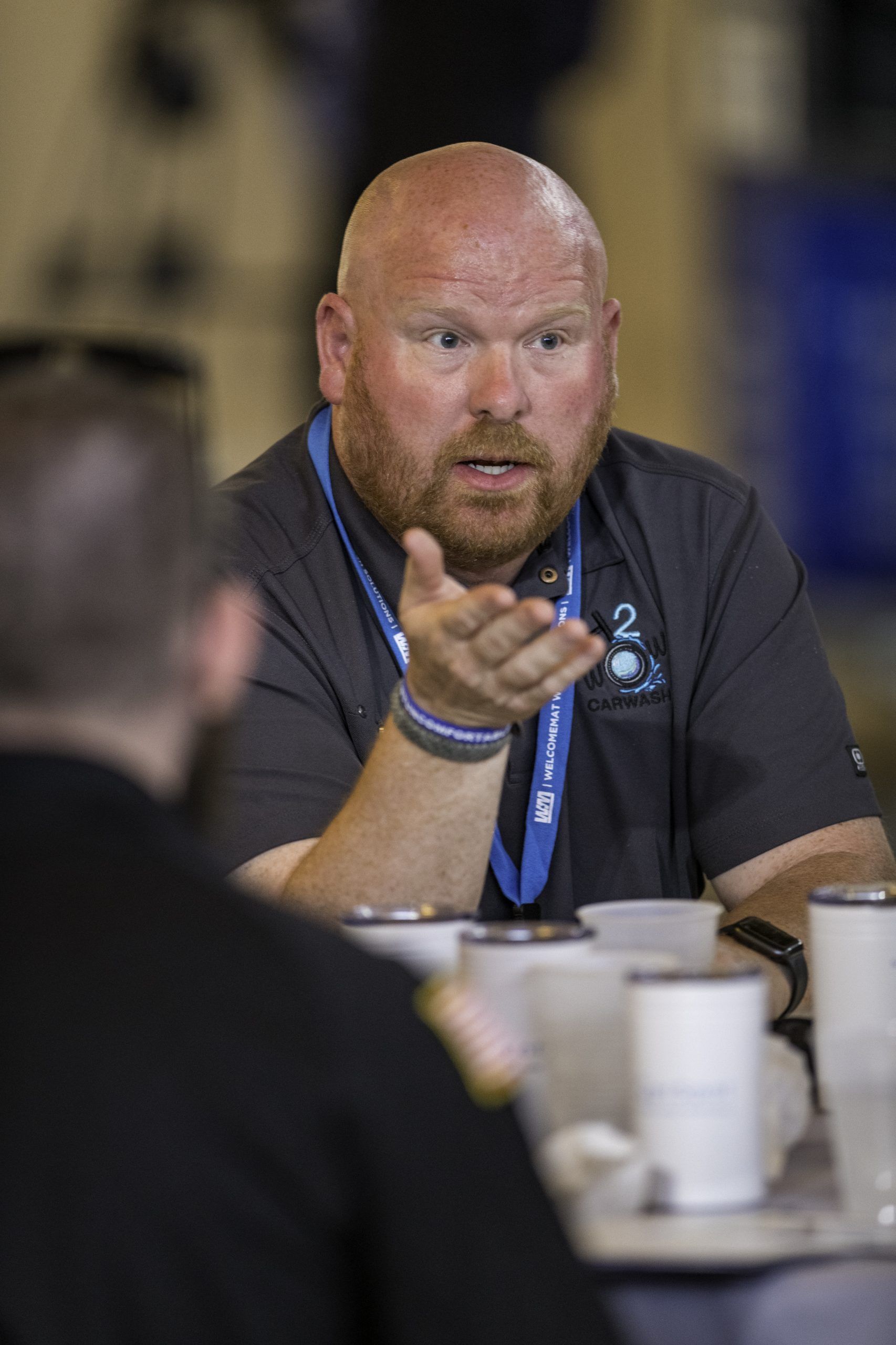 A man with a beard is sitting at a table talking to another man.