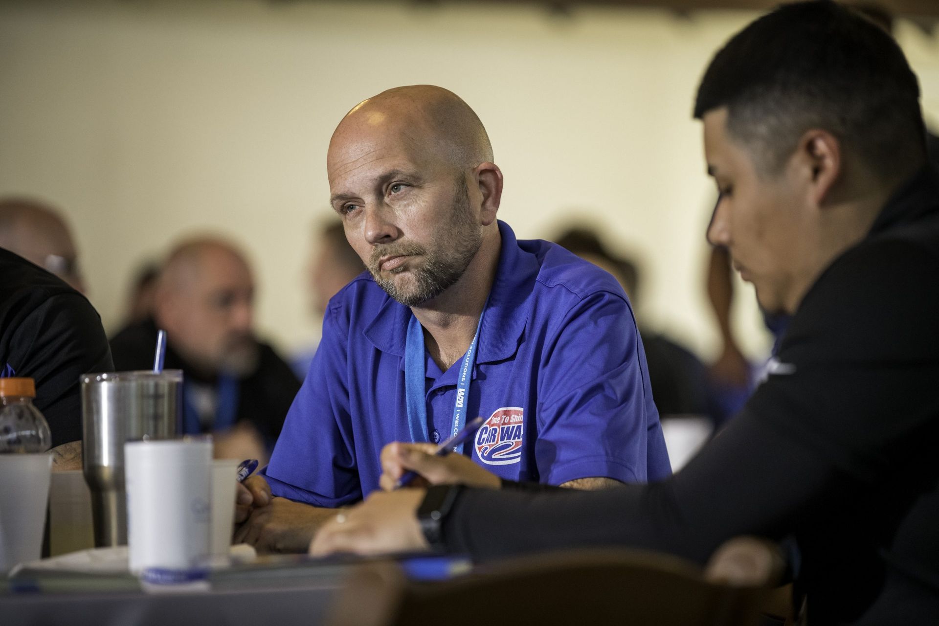 A man in a blue shirt is sitting at a table talking to another man.