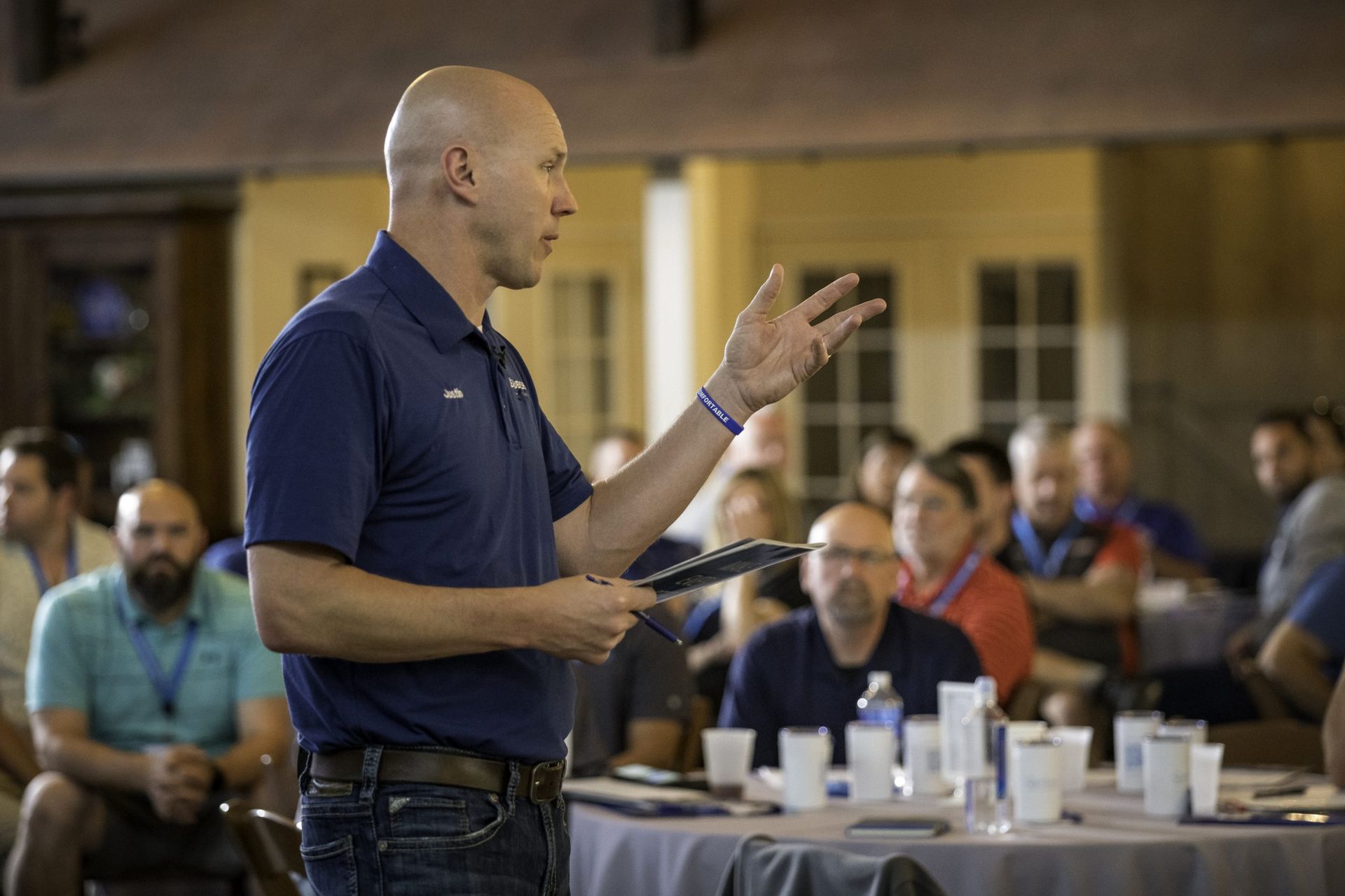 A man is giving a presentation to a group of people sitting at tables.