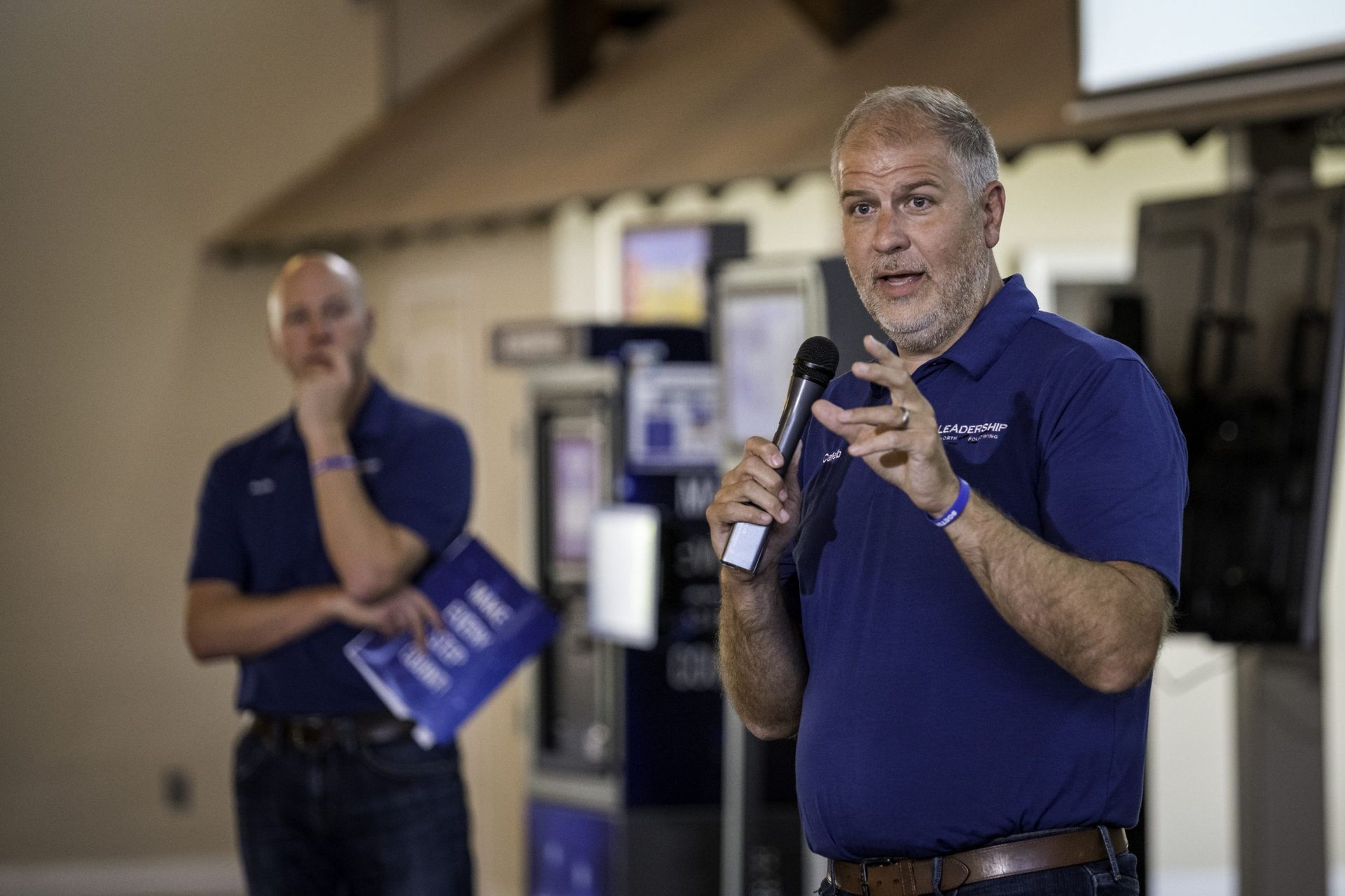 A man is talking into a microphone while another man stands behind him.