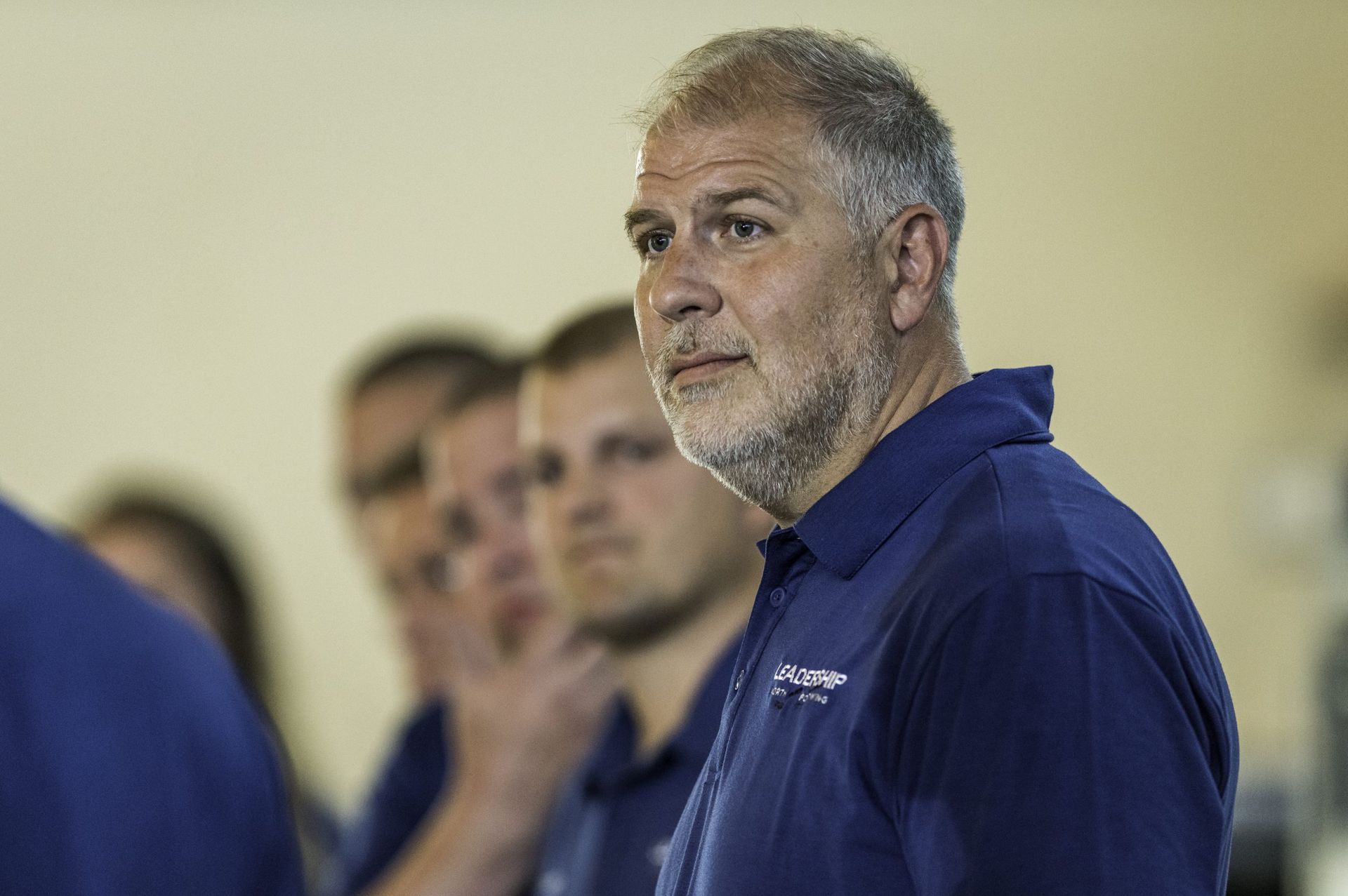 A man with a beard wearing a blue shirt is standing in front of a group of people.