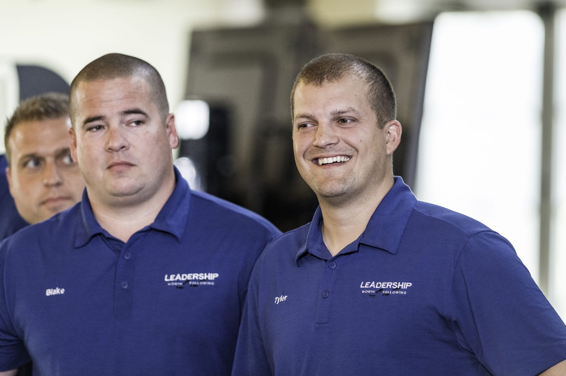 Three men in blue shirts are standing next to each other and smiling.