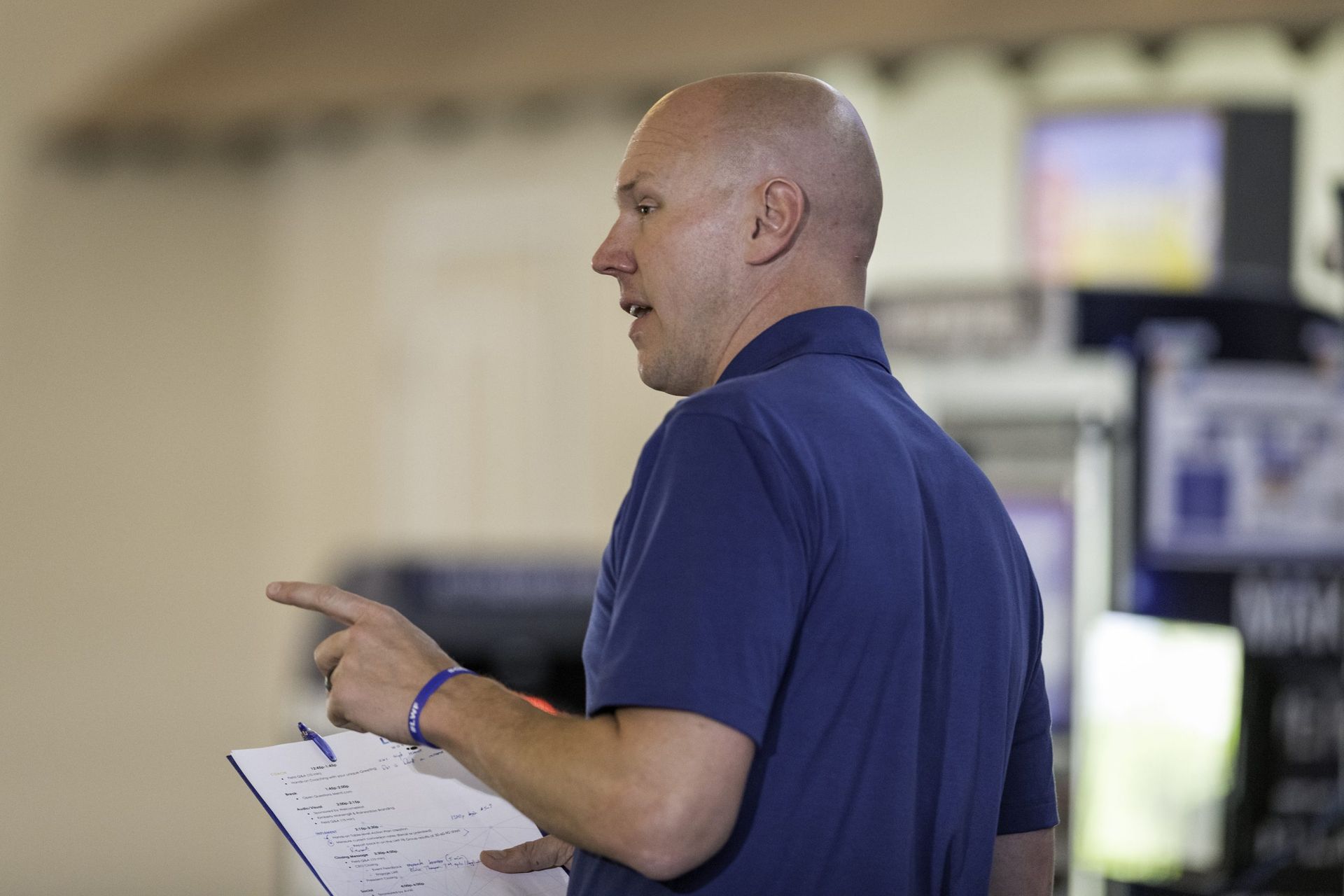 A man in a blue shirt is pointing at something while holding a clipboard.