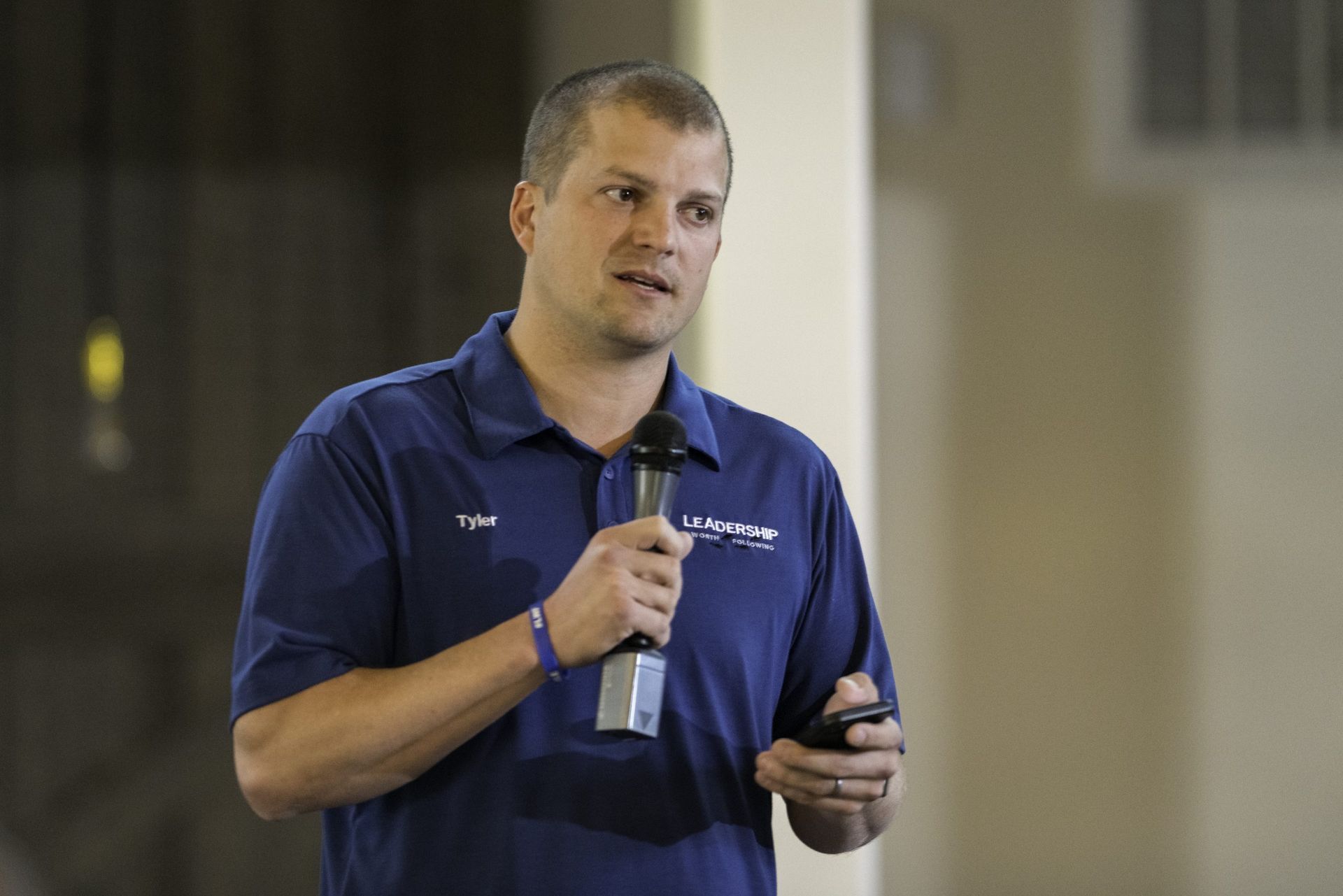 A man in a blue shirt is holding a microphone and a cell phone