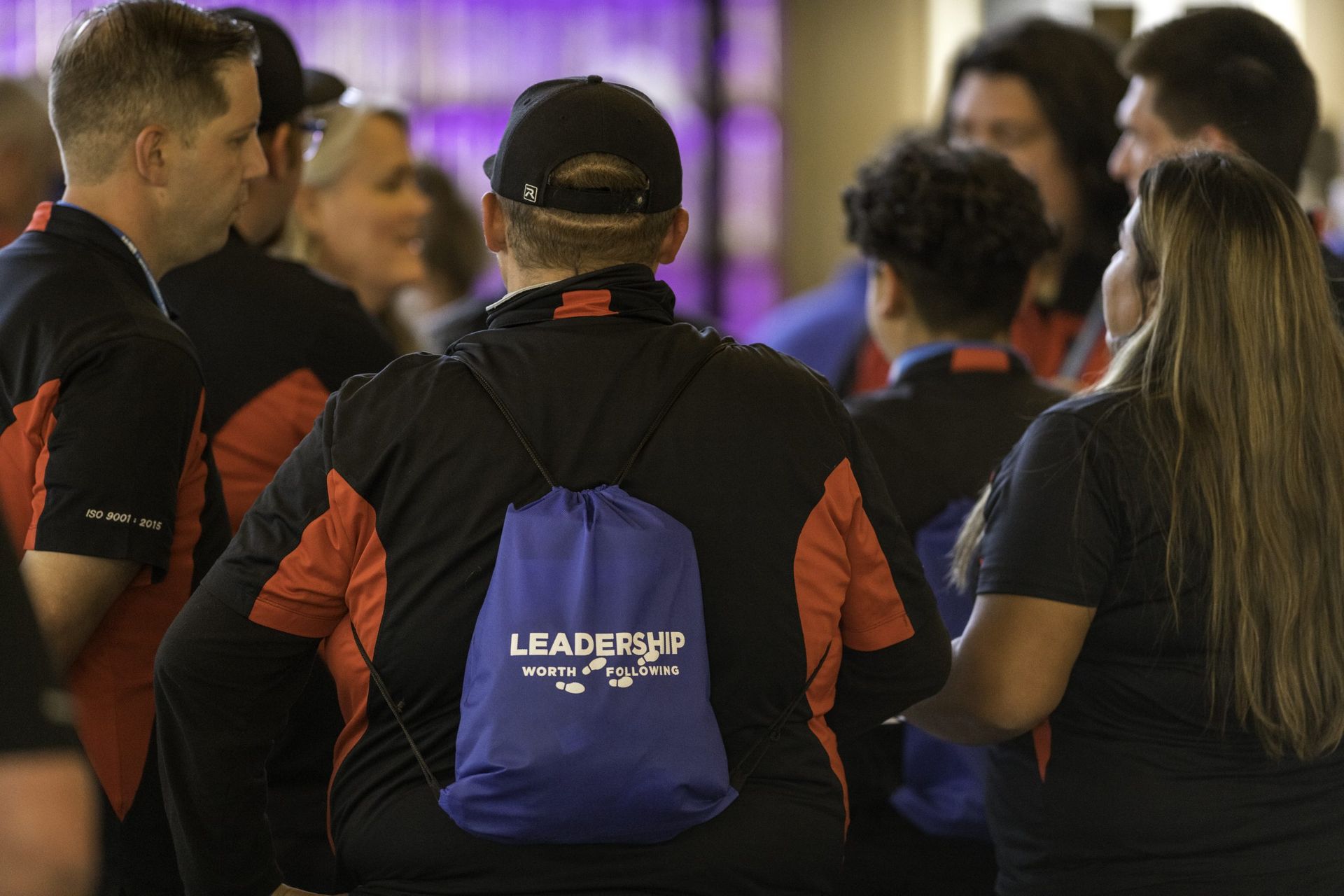 A group of people are standing around a man with a blue backpack that says leadership on it.