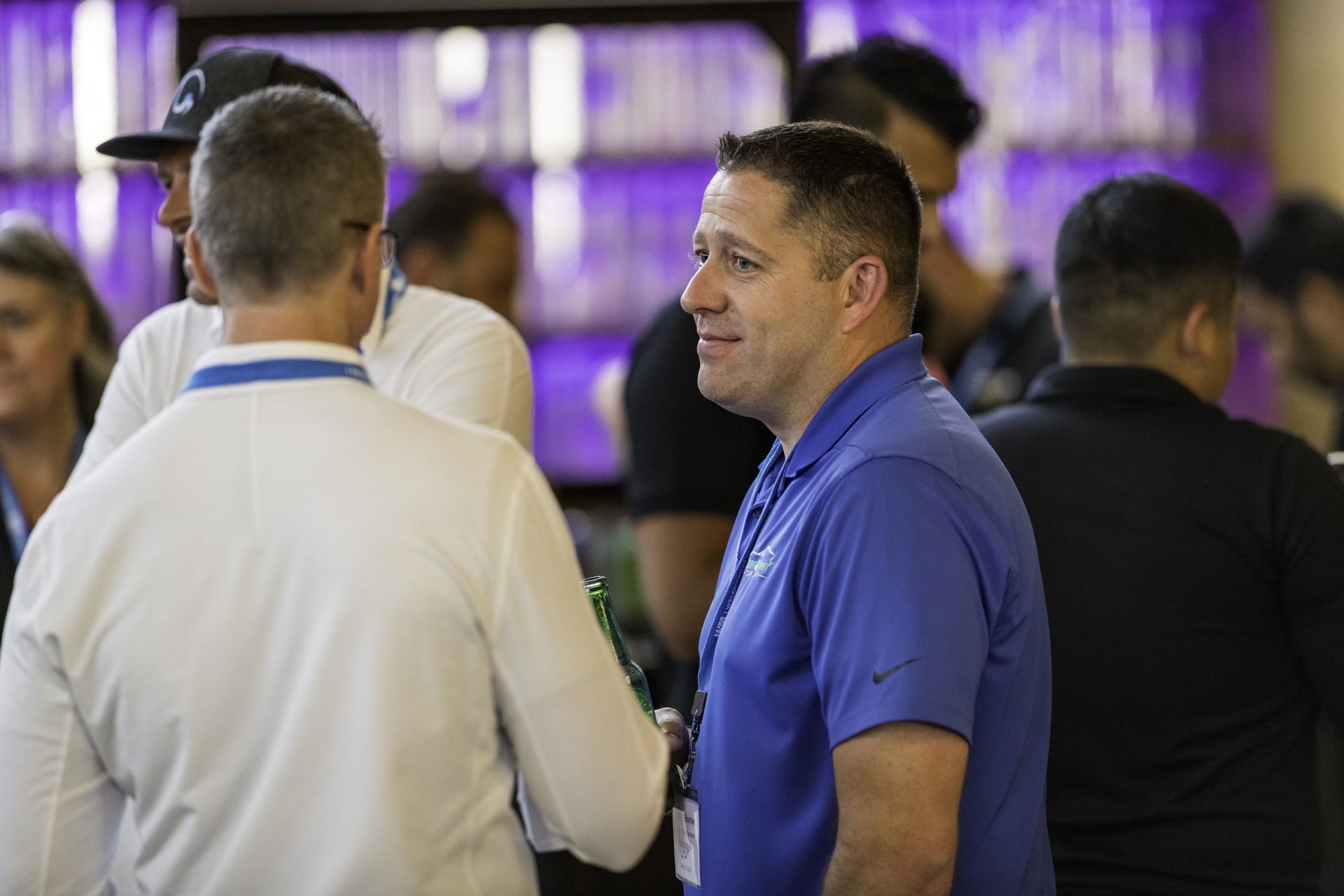 A man in a blue shirt is talking to another man in a crowd of people.
