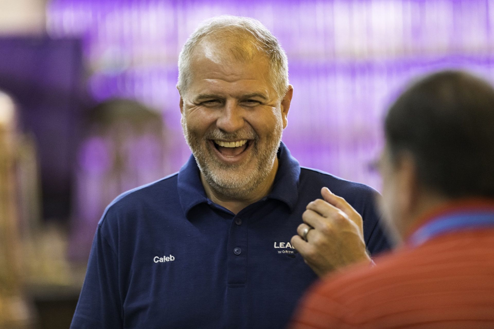 A man with a beard is laughing while talking to another man.