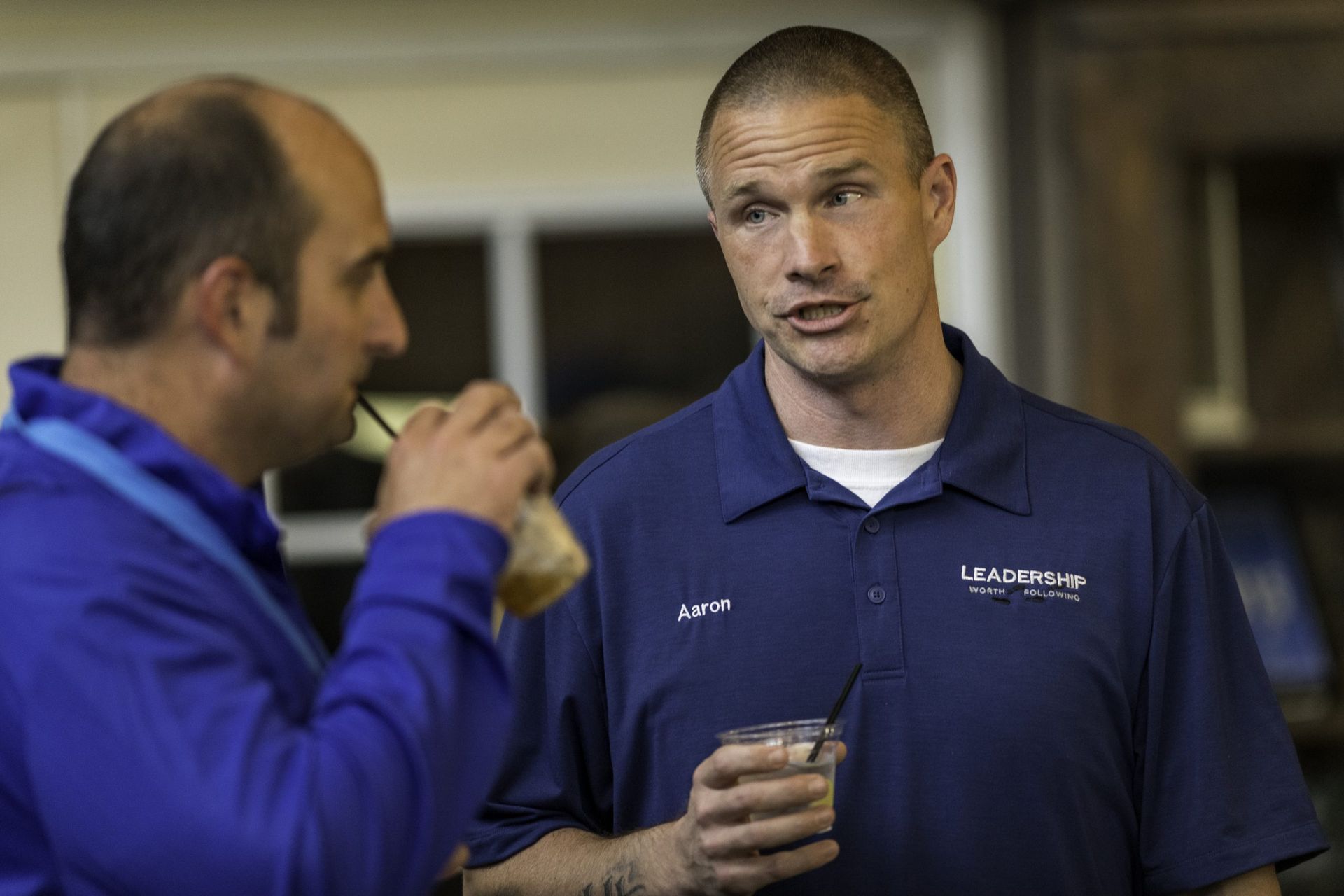 Two men are talking to each other while one of them drinks from a cup.