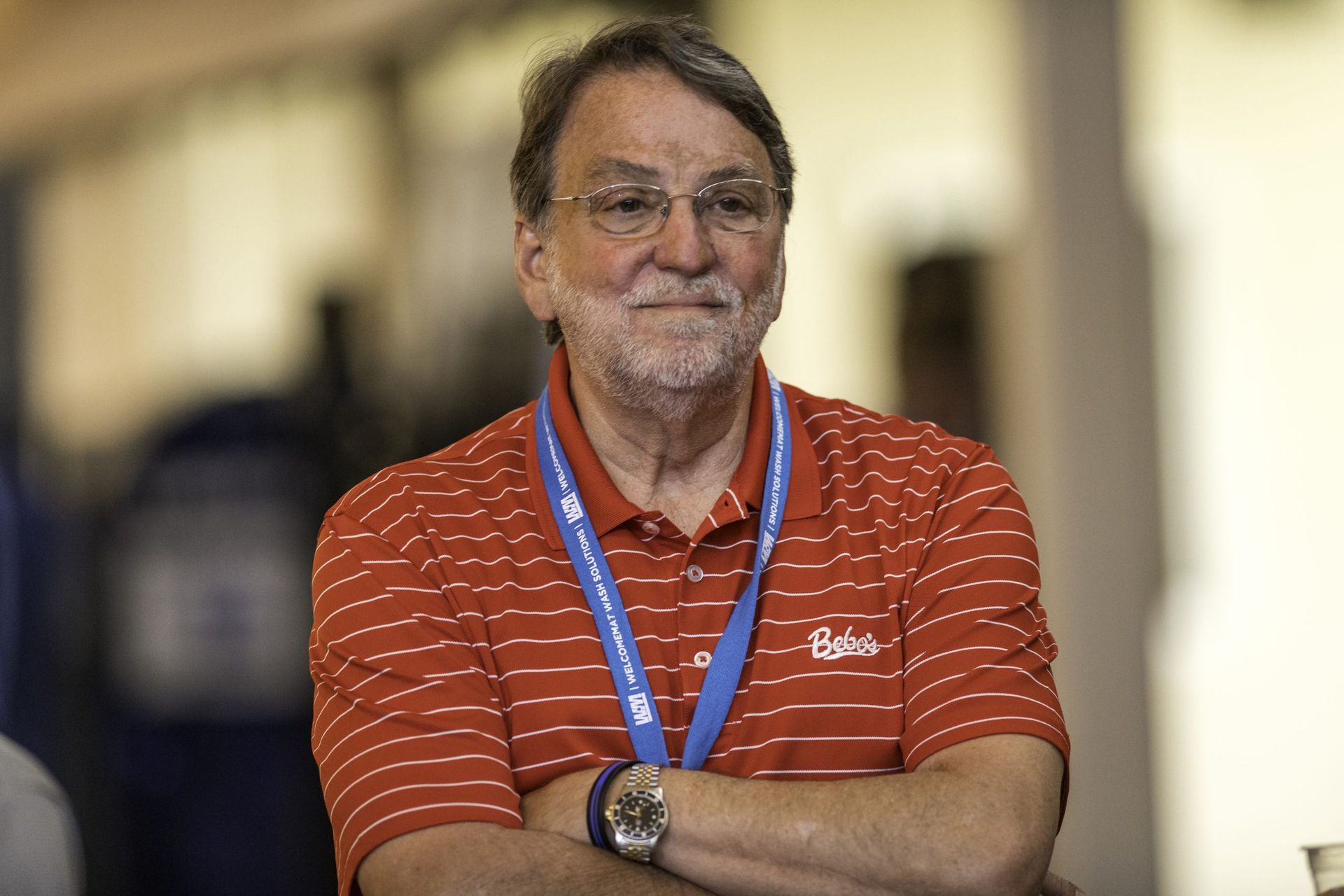 A man with a beard and glasses is wearing a red striped shirt and a blue lanyard around his neck.