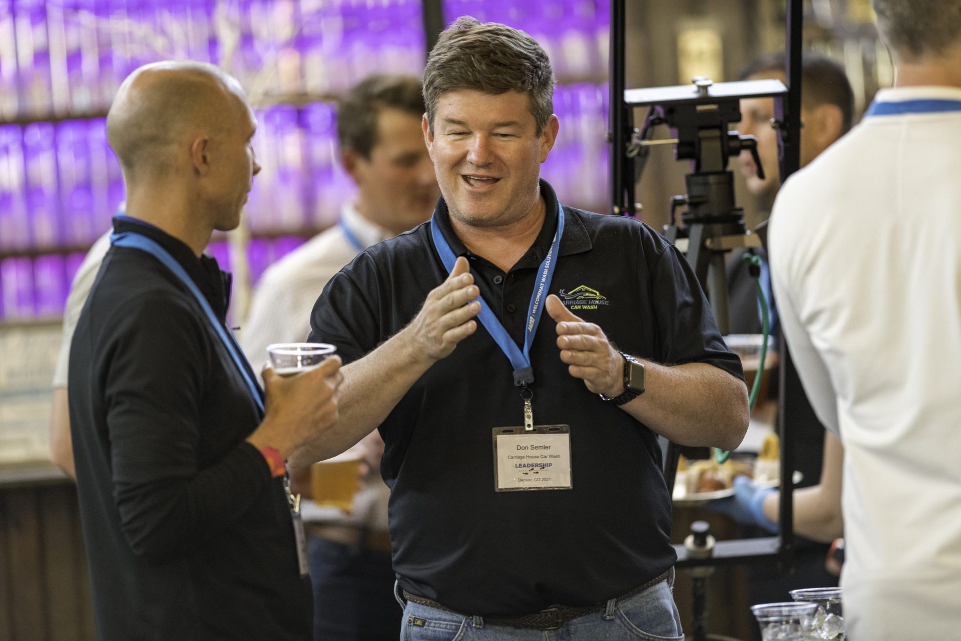 A man wearing a name tag is talking to another man while holding a glass of beer.
