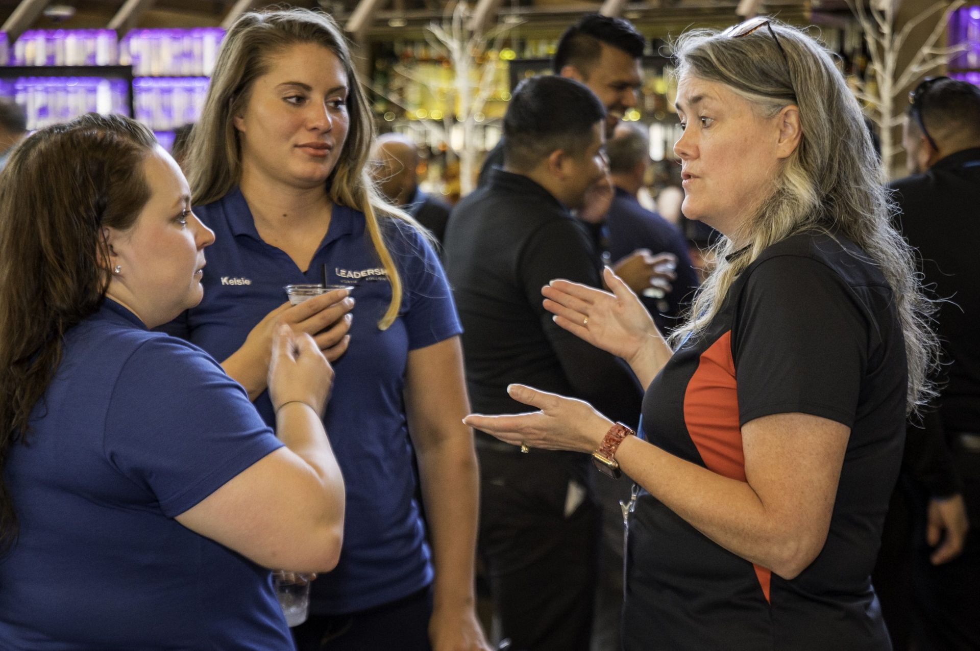 Three women are talking to each other in a crowded room.