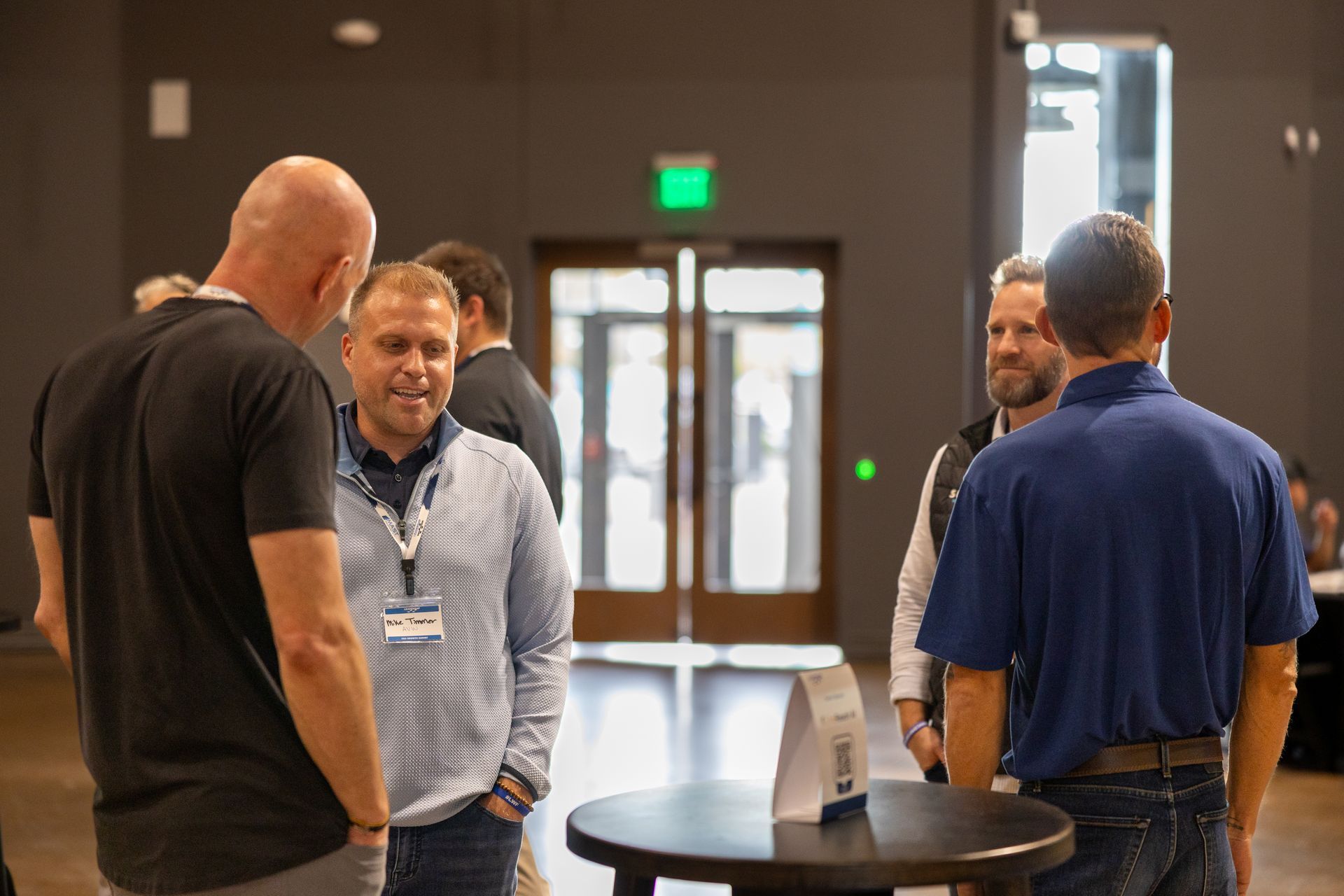 Men talking in small groups at Leadership Worth Following car wash convention. Well-lit, neutral setting.