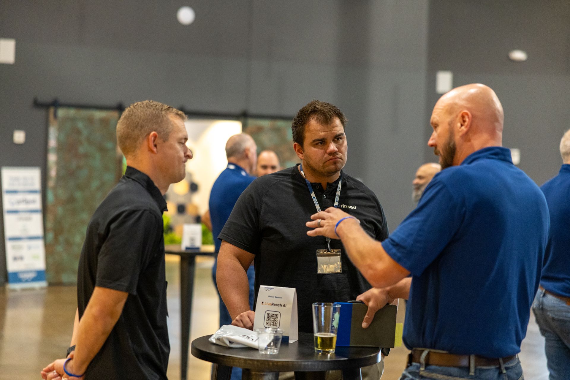 Three men in blue and black shirts converse at Leadership Worth Following car wash event, with name tags.