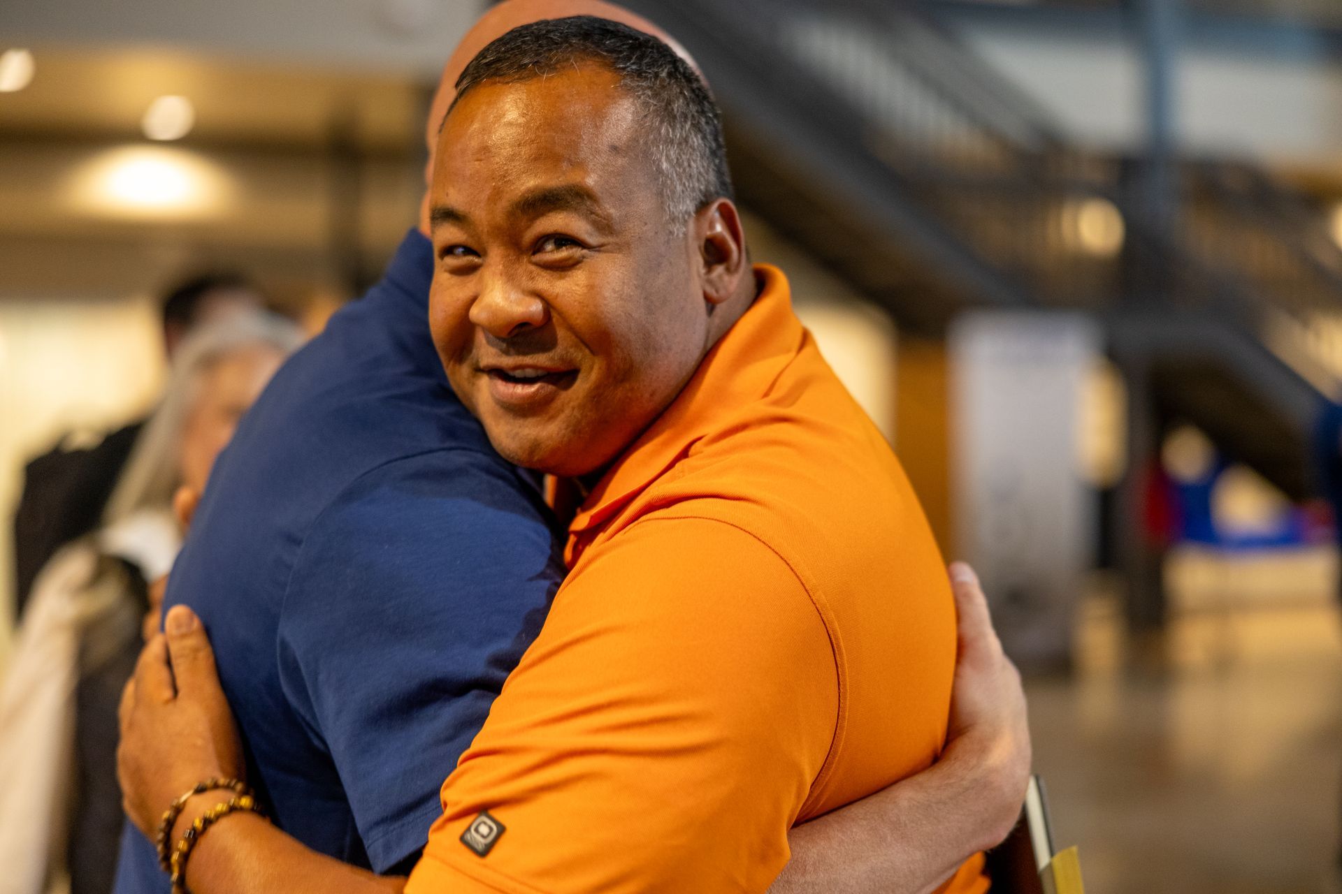 Man in orange shirt smiles while hugging another person at Leadership Worth Following car wash convention