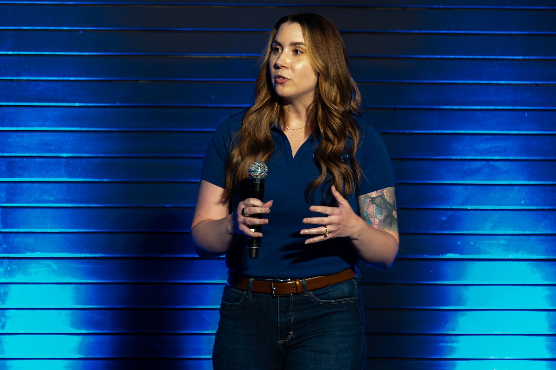 Woman speaking into a microphone, at Leadership Worth Following car wash convention; blue shirt, jeans, blue background.