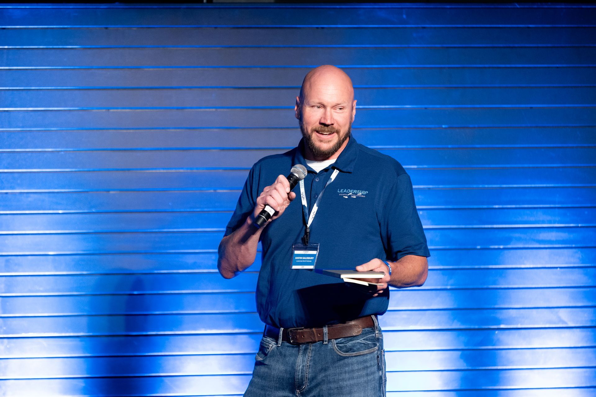 Man with bald head at Leadership Worth Following car wash convention, speaking at a podium with blue background.