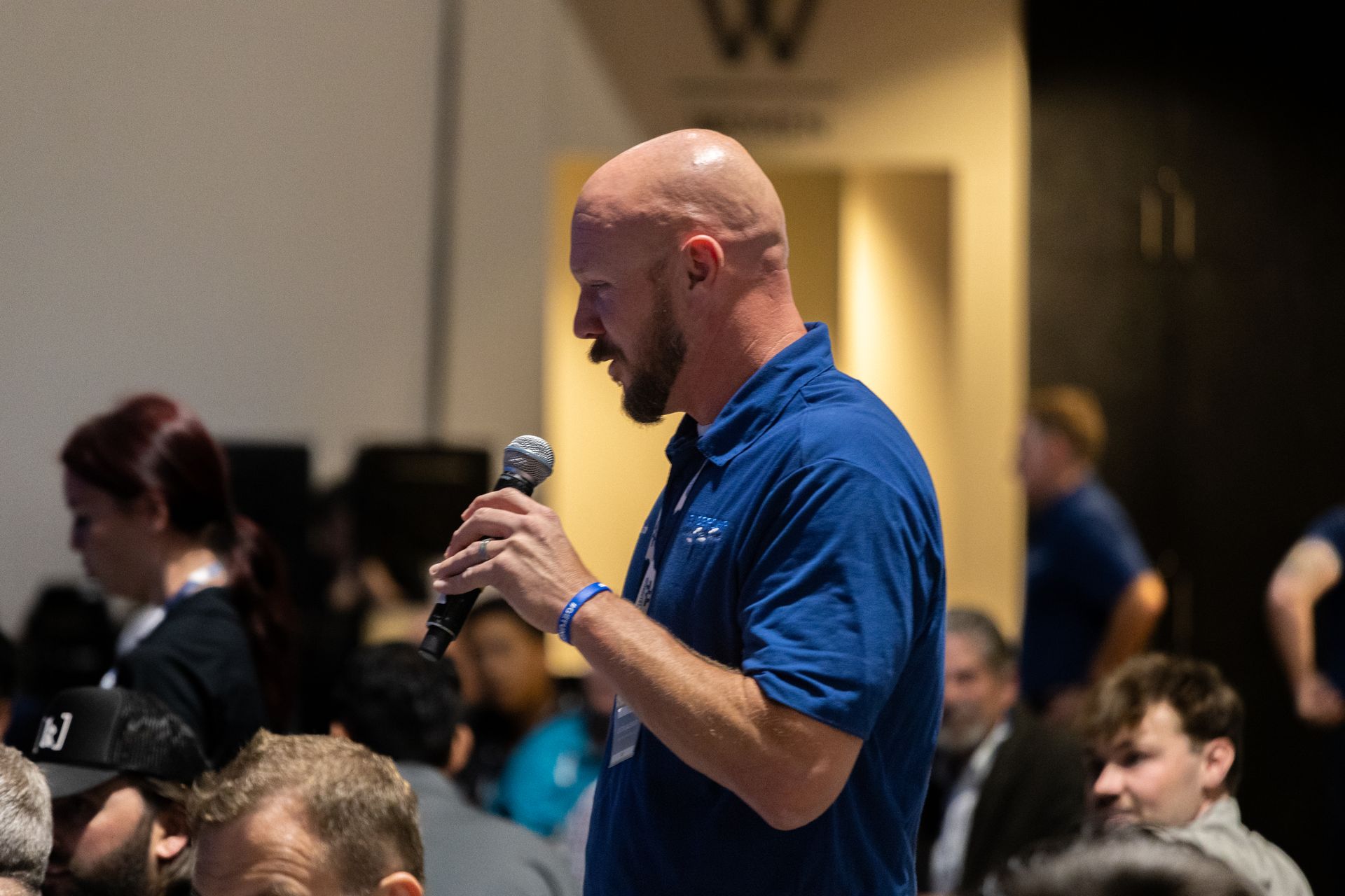 Man with shaved head speaks into microphone at Leadership Worth Following car wash event, wearing a blue shirt.