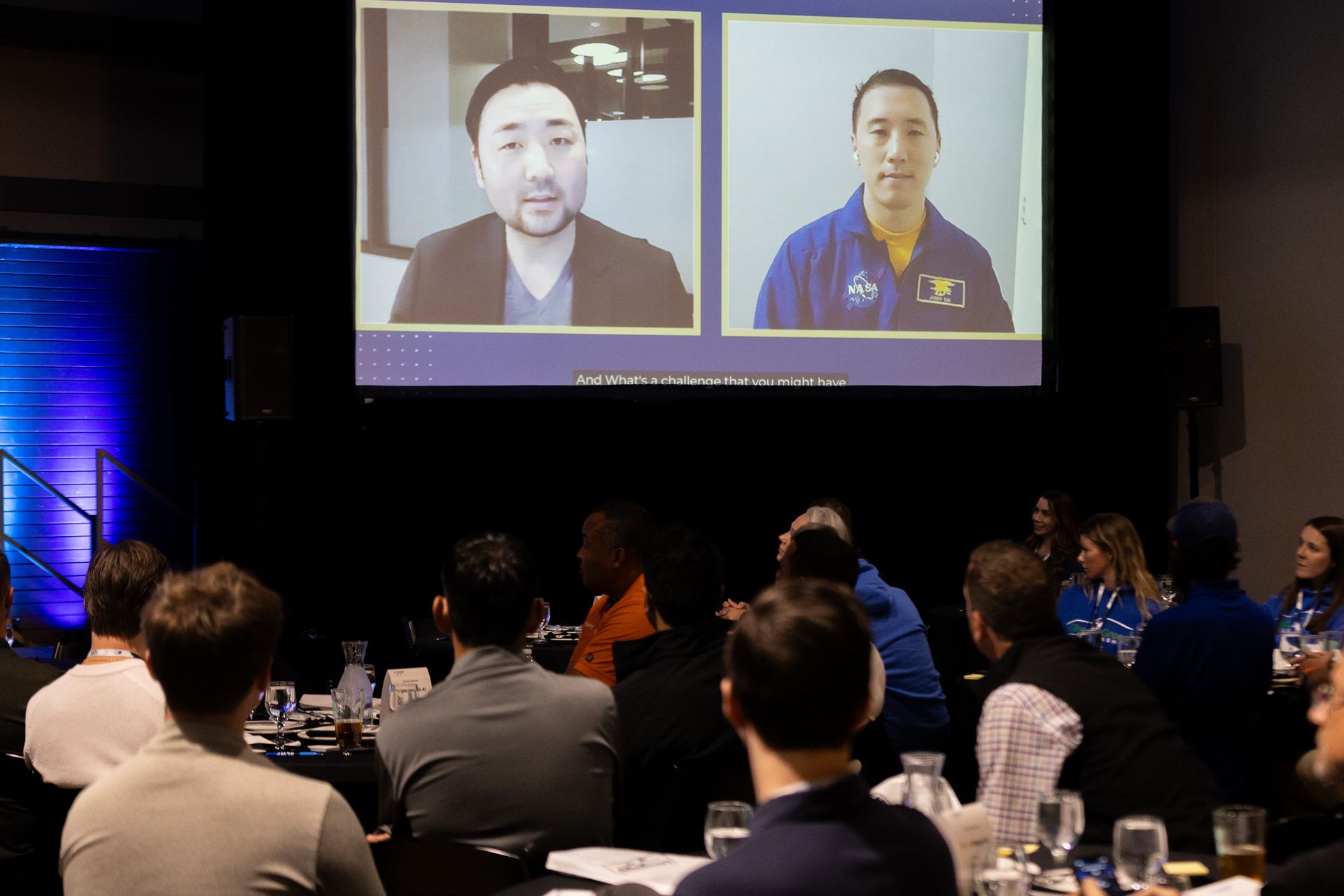 Audience watches two men on a screen during Leadership Worth Following car wash conference. The men appear to be in a video call.