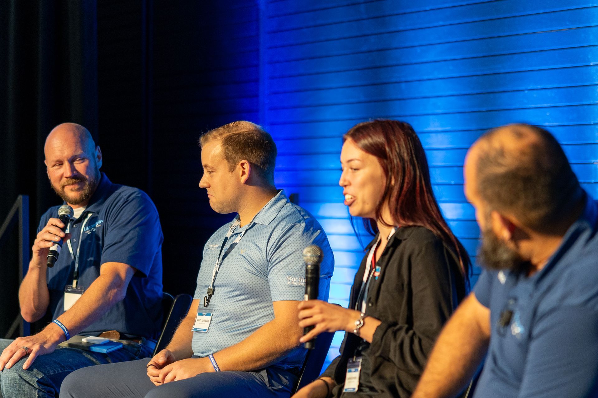 Four people on a stage in blue shirts, holding microphones, participating in a panel discussion.