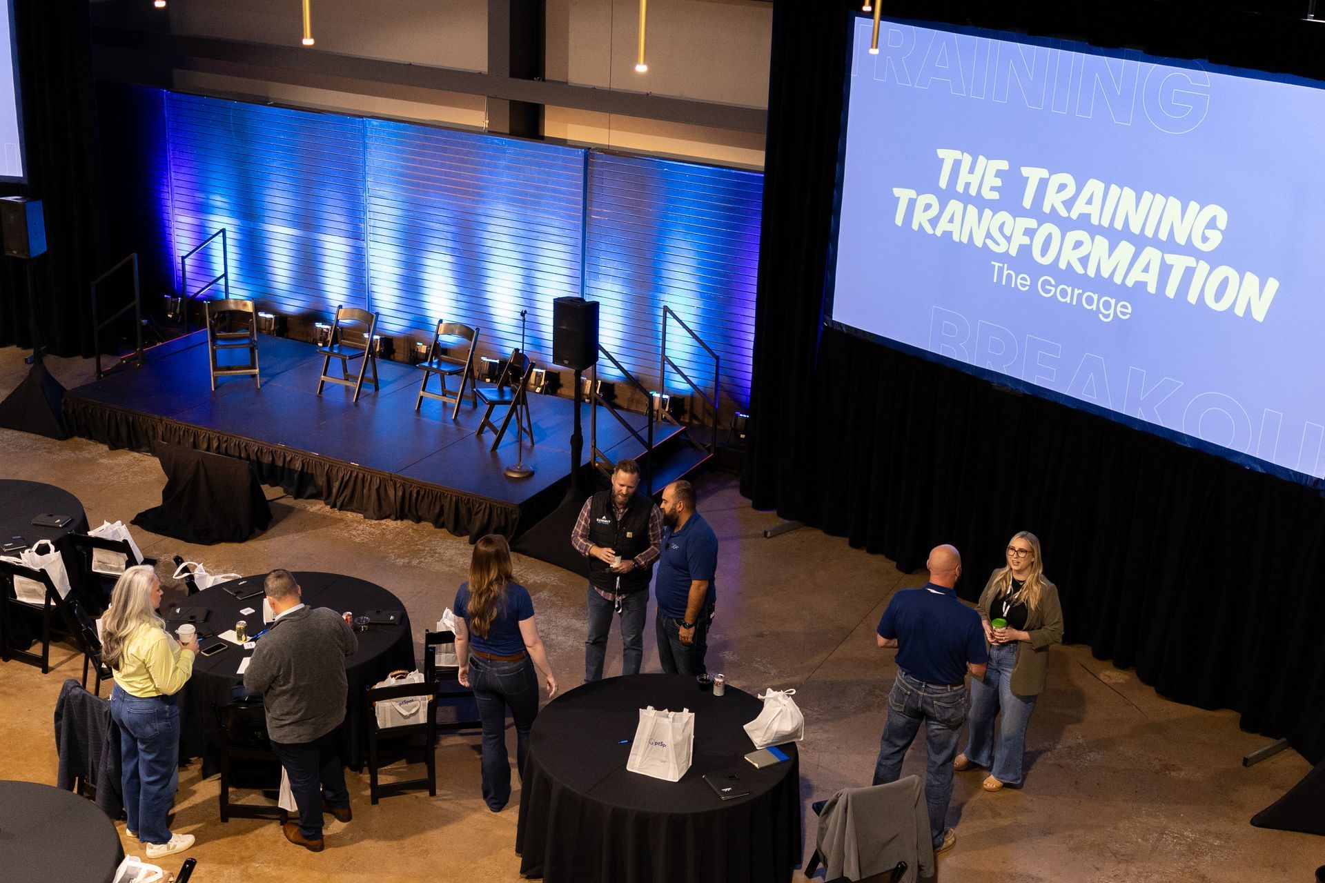 Conference room with stage and people networking. The Training Transformation is on screen.