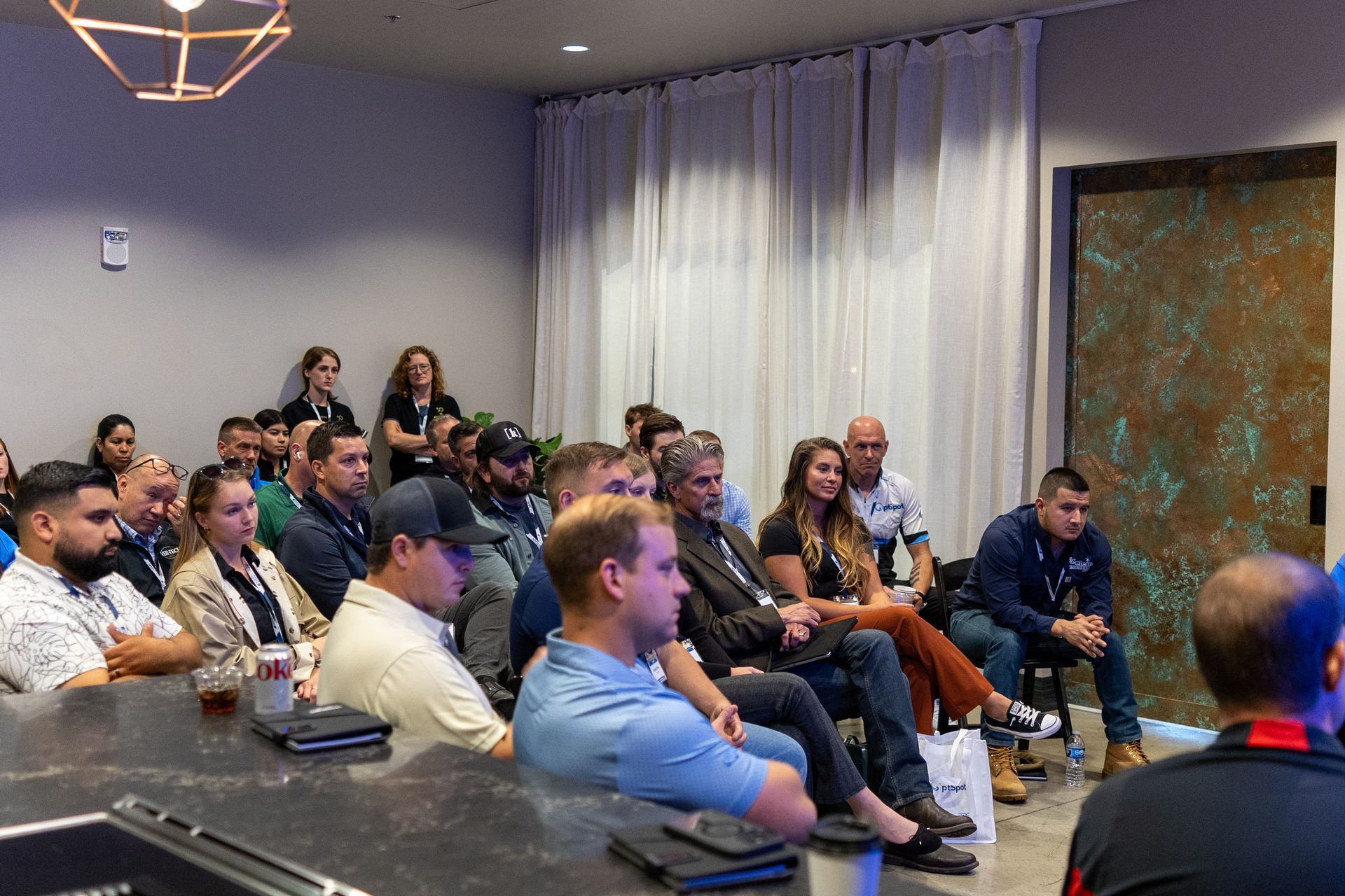 Audience members attentively listening to a presentation in a modern room with a bar.