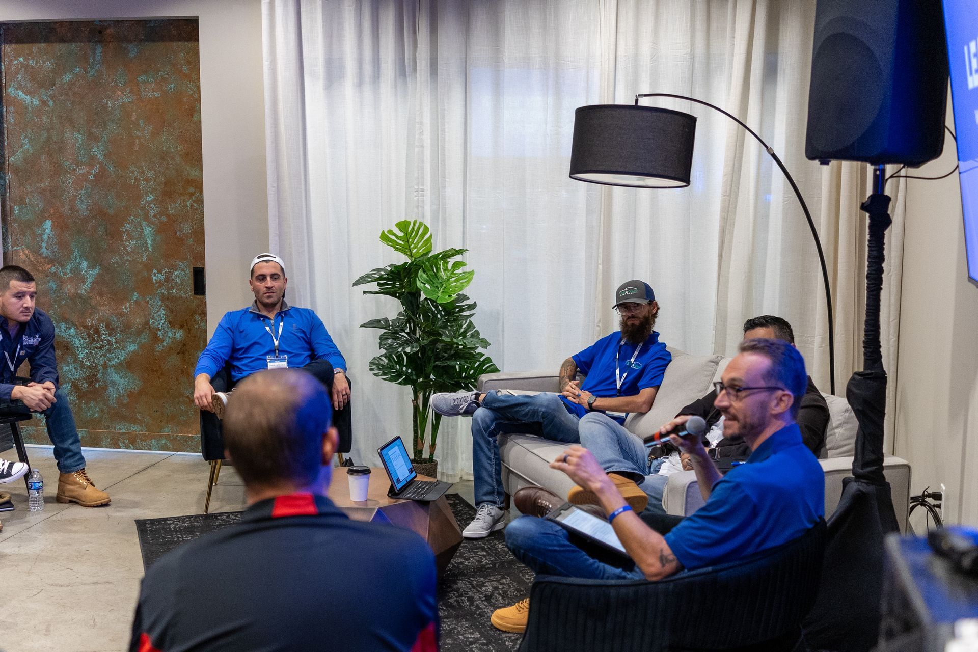 Panel discussion: Six people sit and talk, mics, speaker, curtained backdrop.