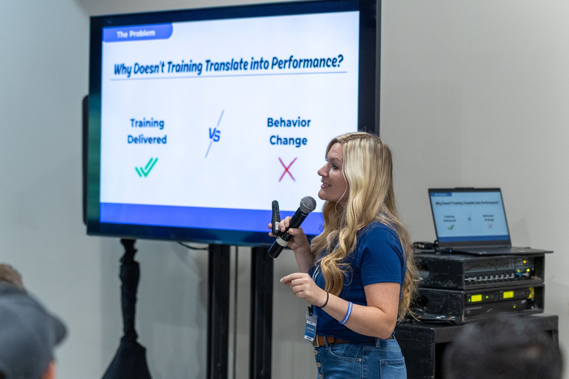 Woman presenting at a conference, pointing at a screen that says