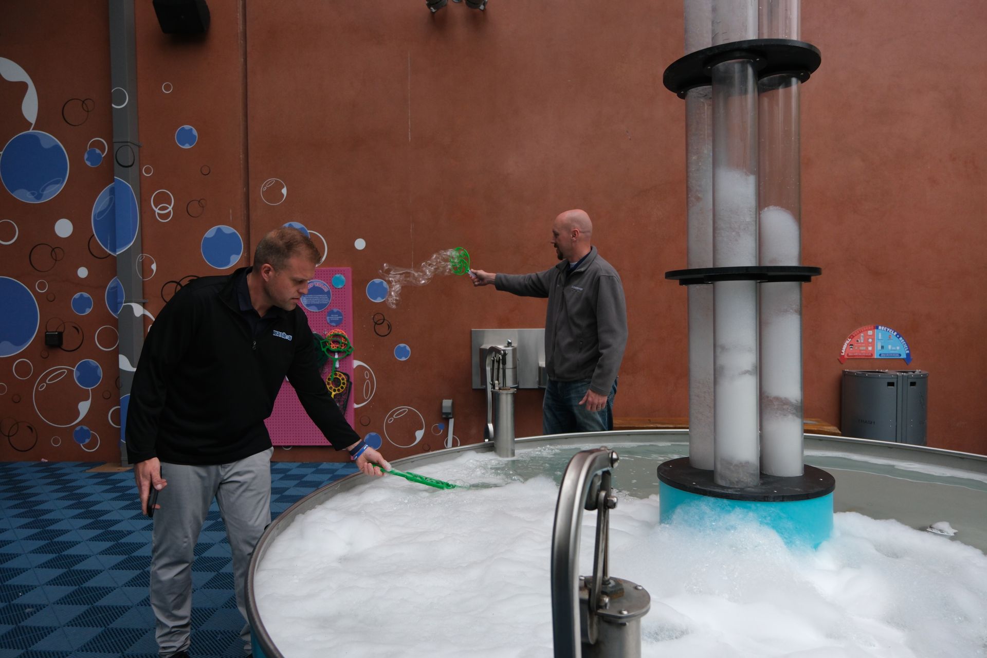 Two men are playing with soap bubbles in a room.