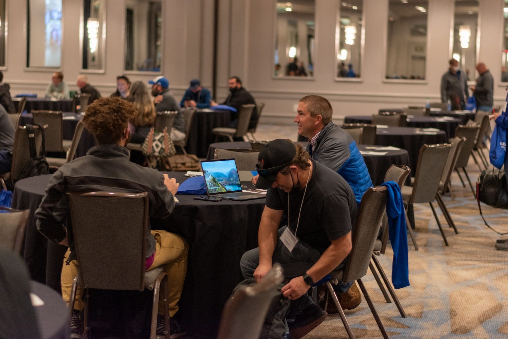 A group of people are sitting around tables in a conference room