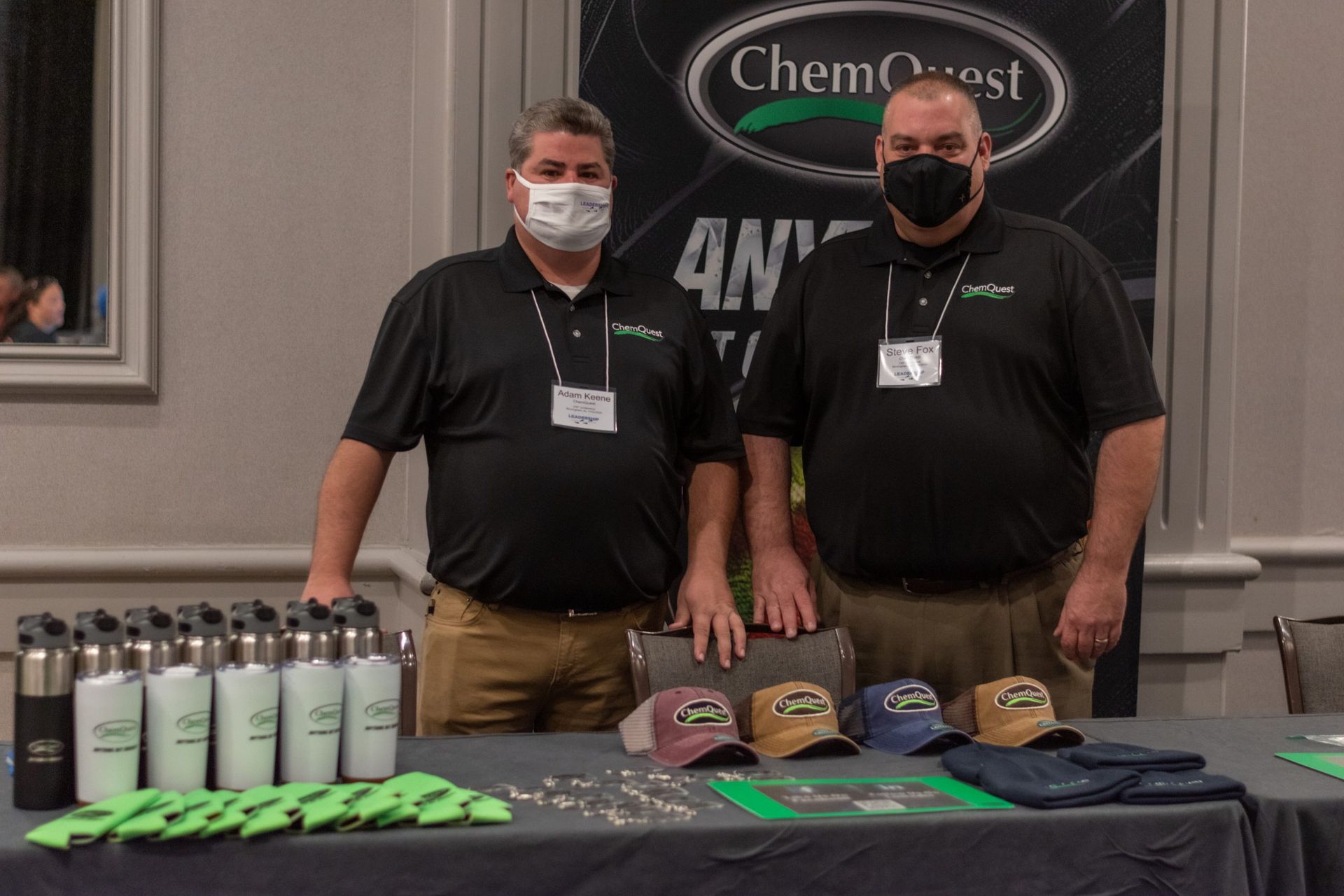 Two men wearing masks stand in front of a chemquest sign