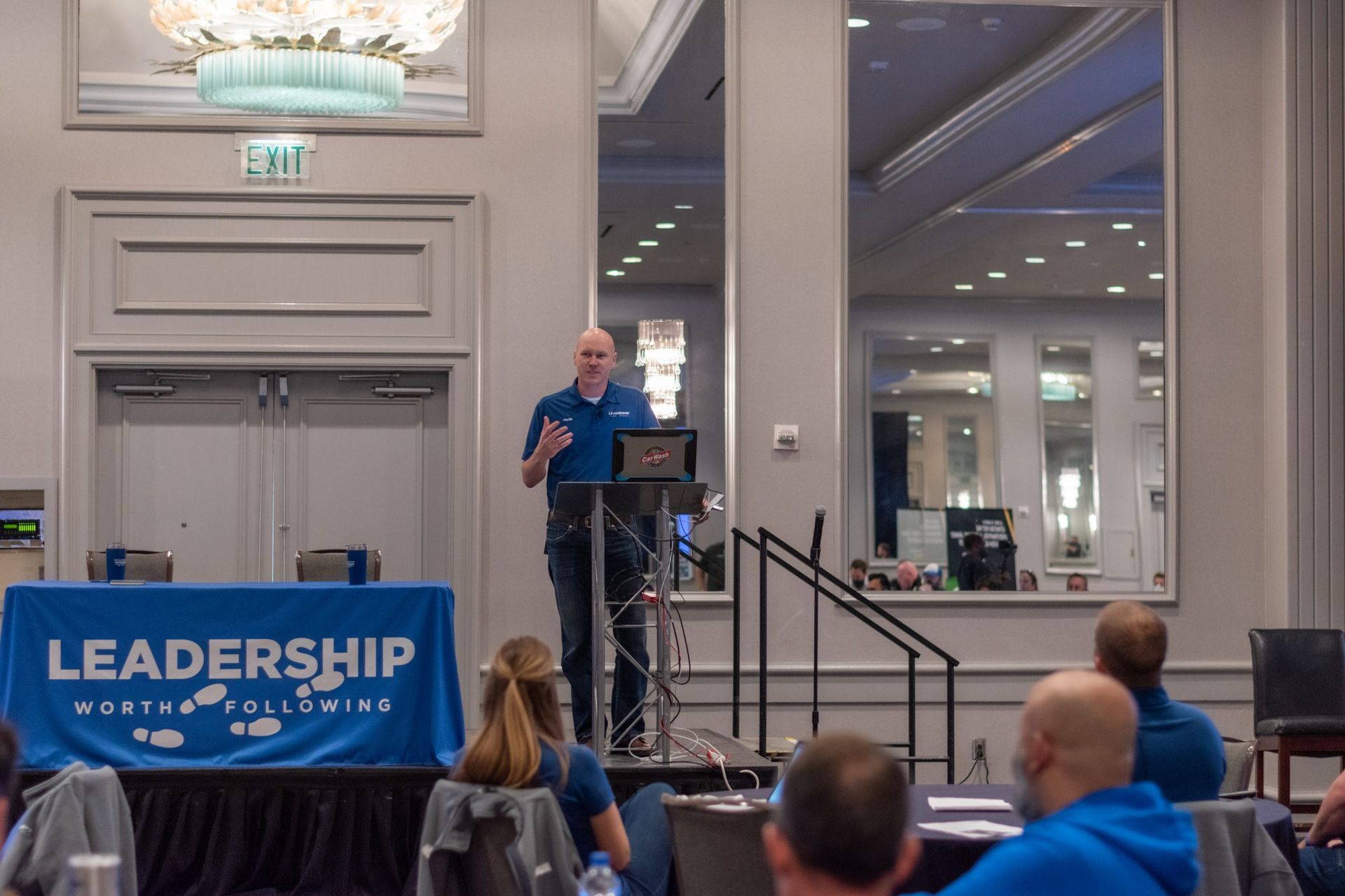 A man stands at a podium in front of a blue table cloth that says leadership