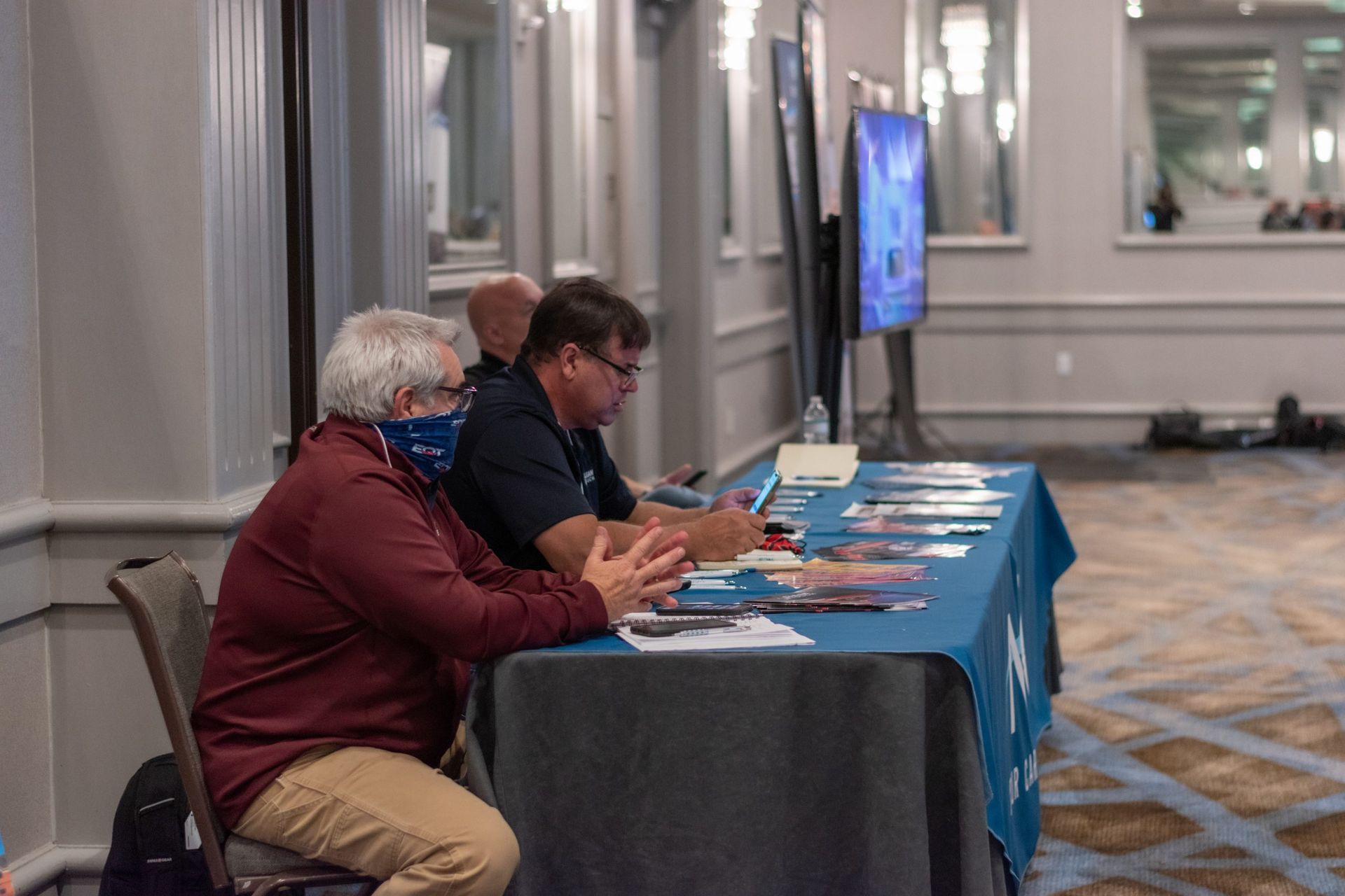 Two men wearing face masks are sitting at a table.