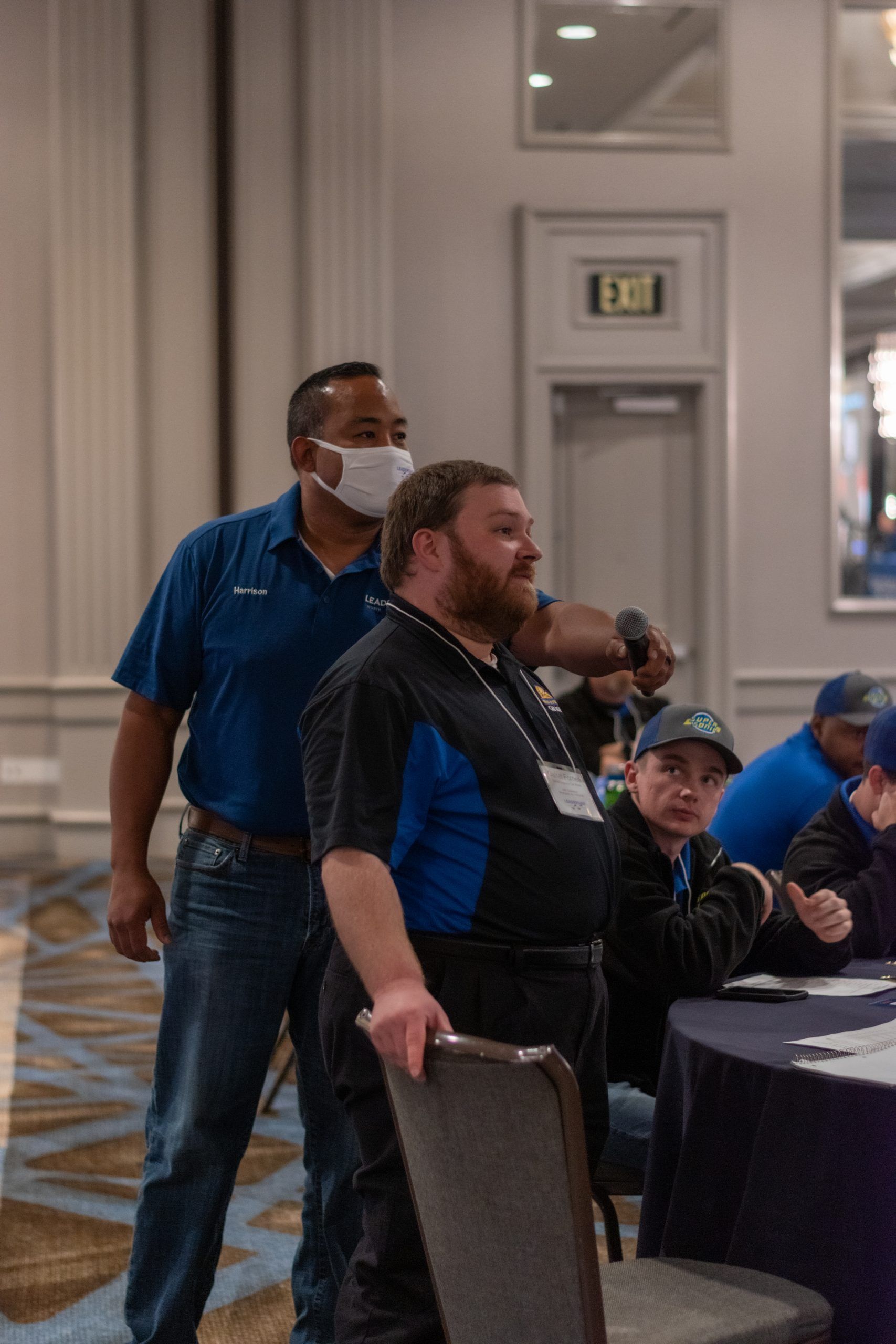 A man wearing a mask is standing next to another man in a room.