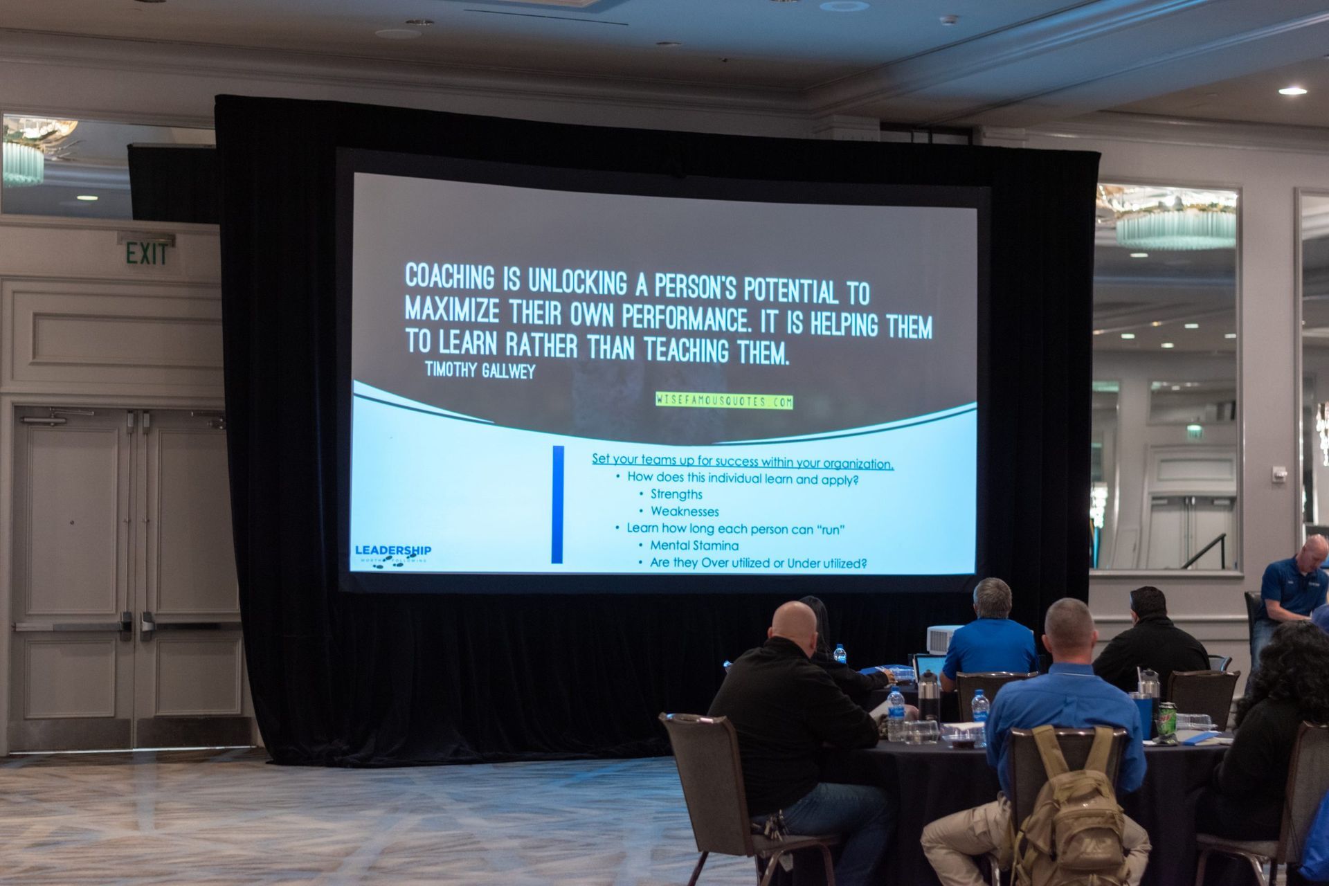 A group of people are sitting in front of a large screen that says coaching