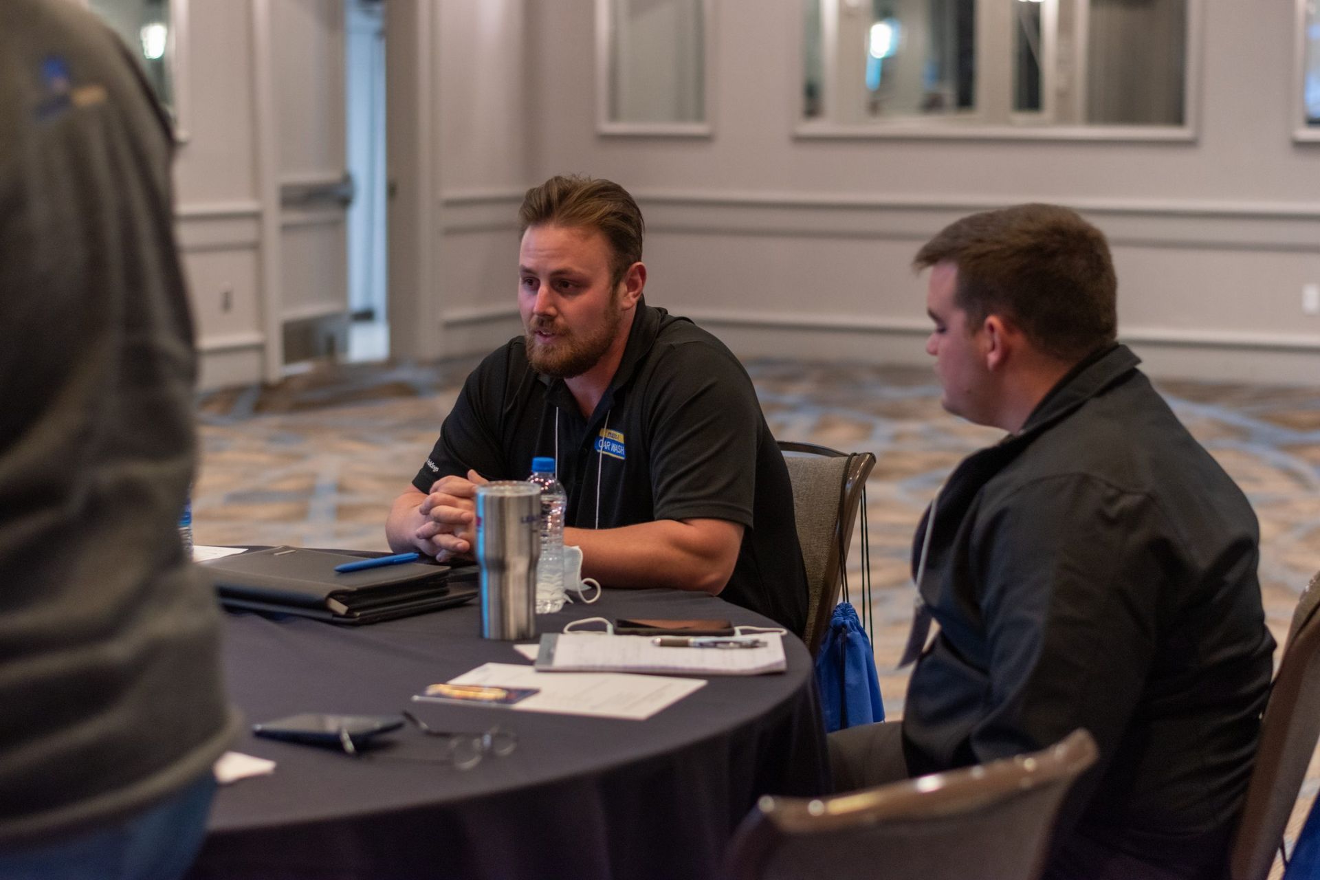 Two men are sitting at a table talking to each other.
