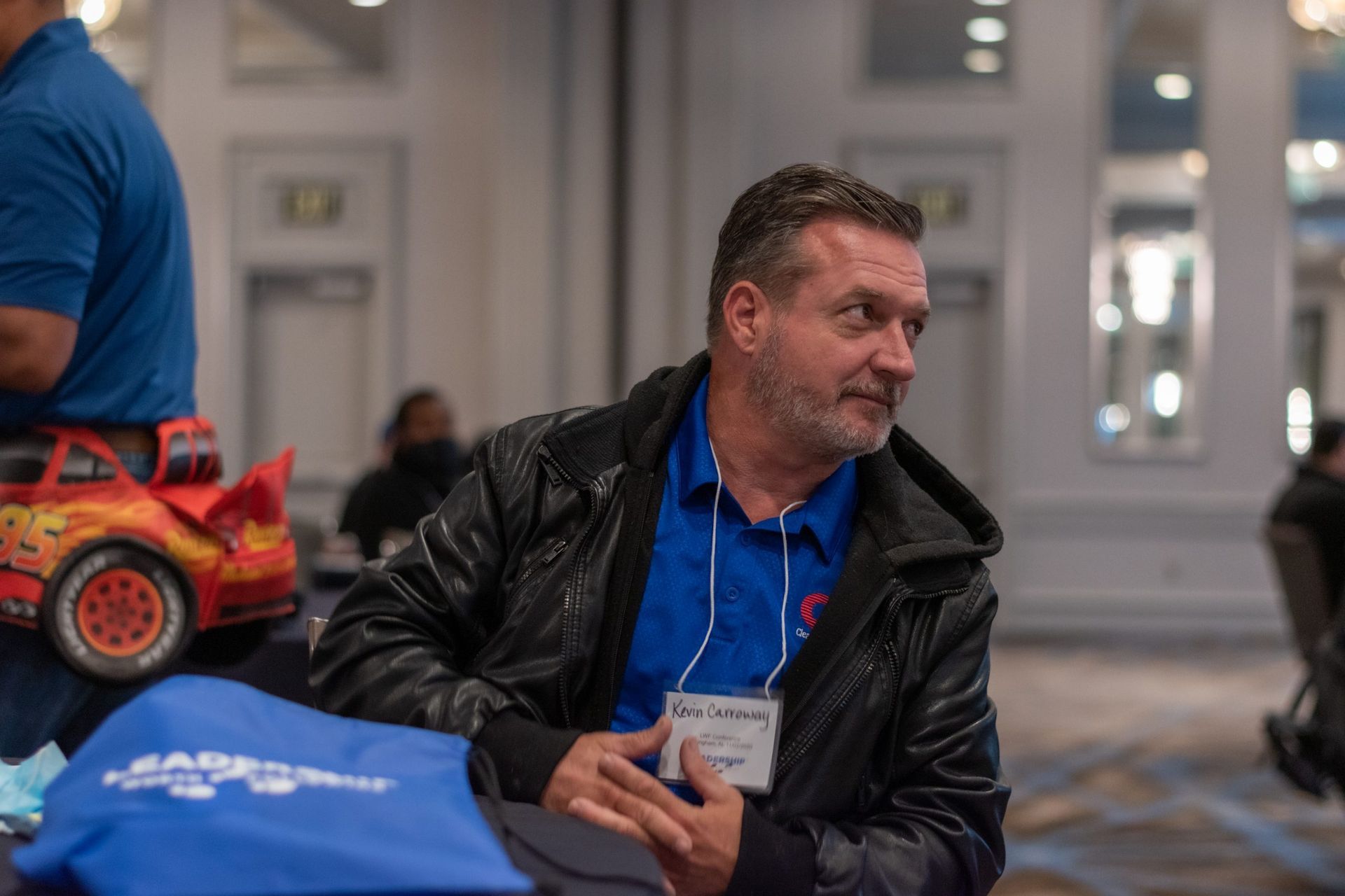 A man is sitting at a table with a toy car in the background.