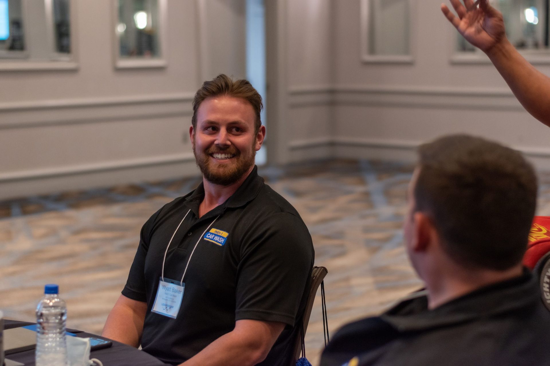 A man in a black shirt is sitting at a table talking to another man.