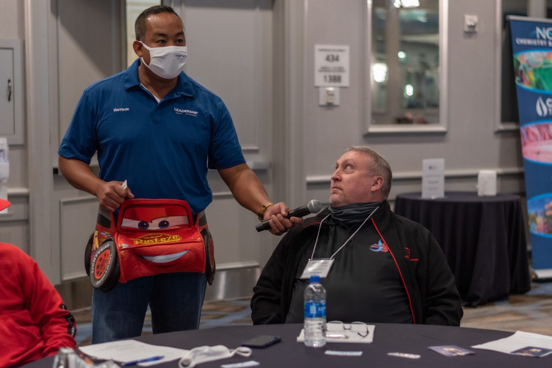 A man wearing a mask is holding a toy car in front of a man in a wheelchair.